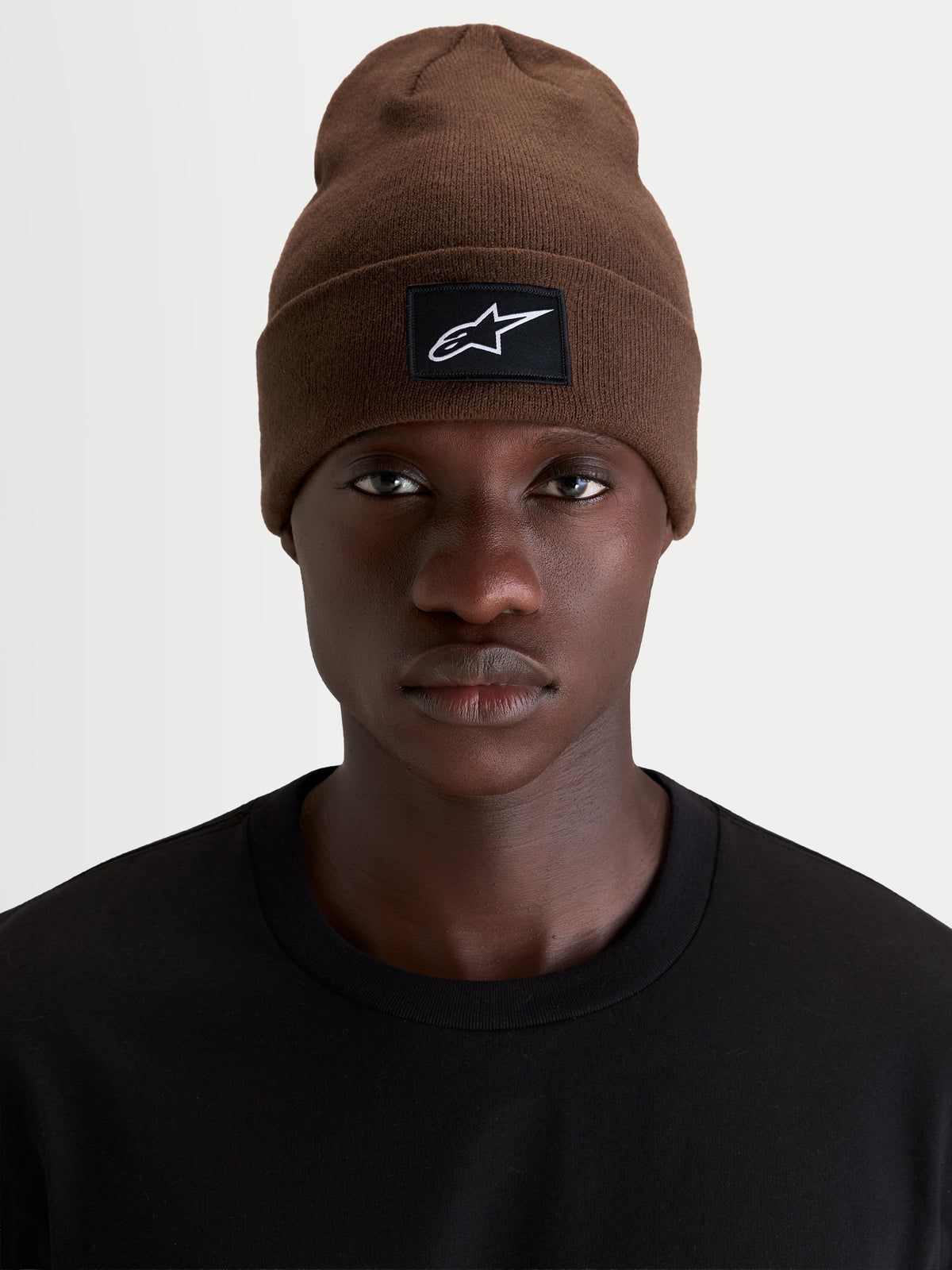 Alpinestars Augment Cuff Beanie, brun sportswear-beanie med vævet Alpinestars-logopatch på opslaget, båret af model i sort t-shirt