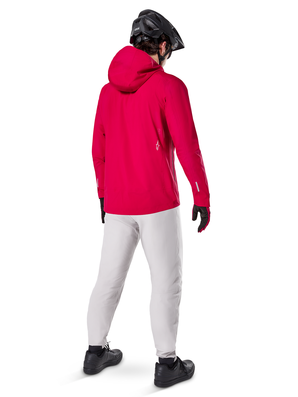 Alpinestars A-Dura Elite vandtæt jakke, Red Fluo, set bagfra i trekvart profil, båret med lysegrå bukser og sort MTB-hjelm, har hætte og reflekterende detaljer, højtydende cykelregnjakke til trail-kørsel