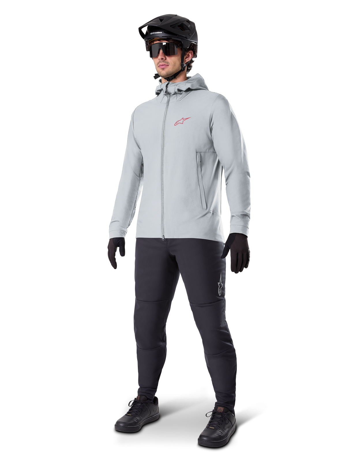 Alpinestars A-Dura Thermal Jacket i Titanium, lysegrå cykeljakke med hætte, rødt Alpinestars-logo på brystet, båret af en mand med sort MTB-hjelm, solbriller, mørkegrå bukser og sorte handsker, professionelt mountainbike-udstyr