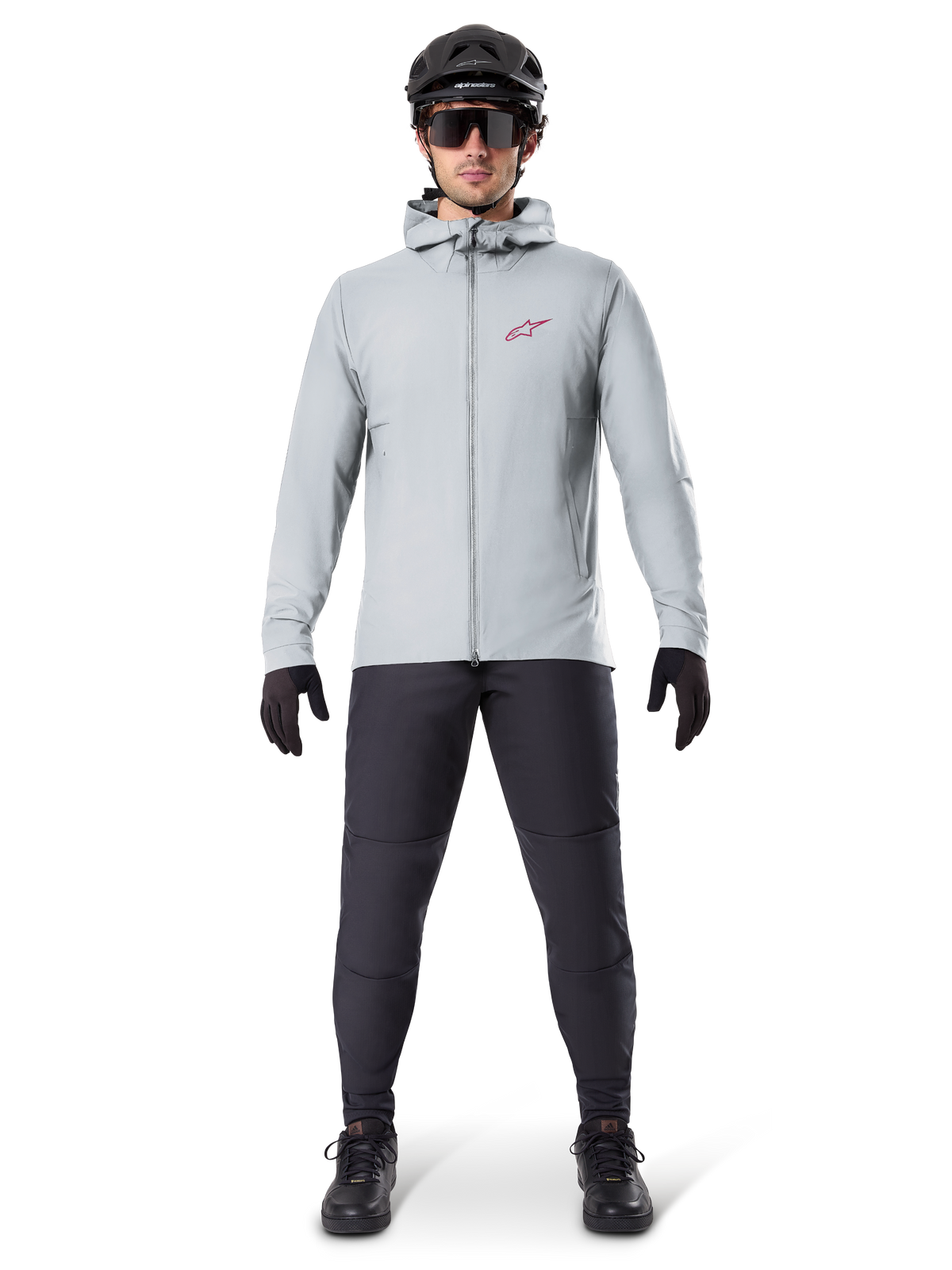 Alpinestars A-Dura Thermal Jacket, titaniumgrå, cykeljakke båret med sorte mountainbikebukser, handsker og hjelm, med et lille rødt stjernelogo på brystet og gennemgående lynlås, letvægtsisoleret udstyr til terrænkørsel.