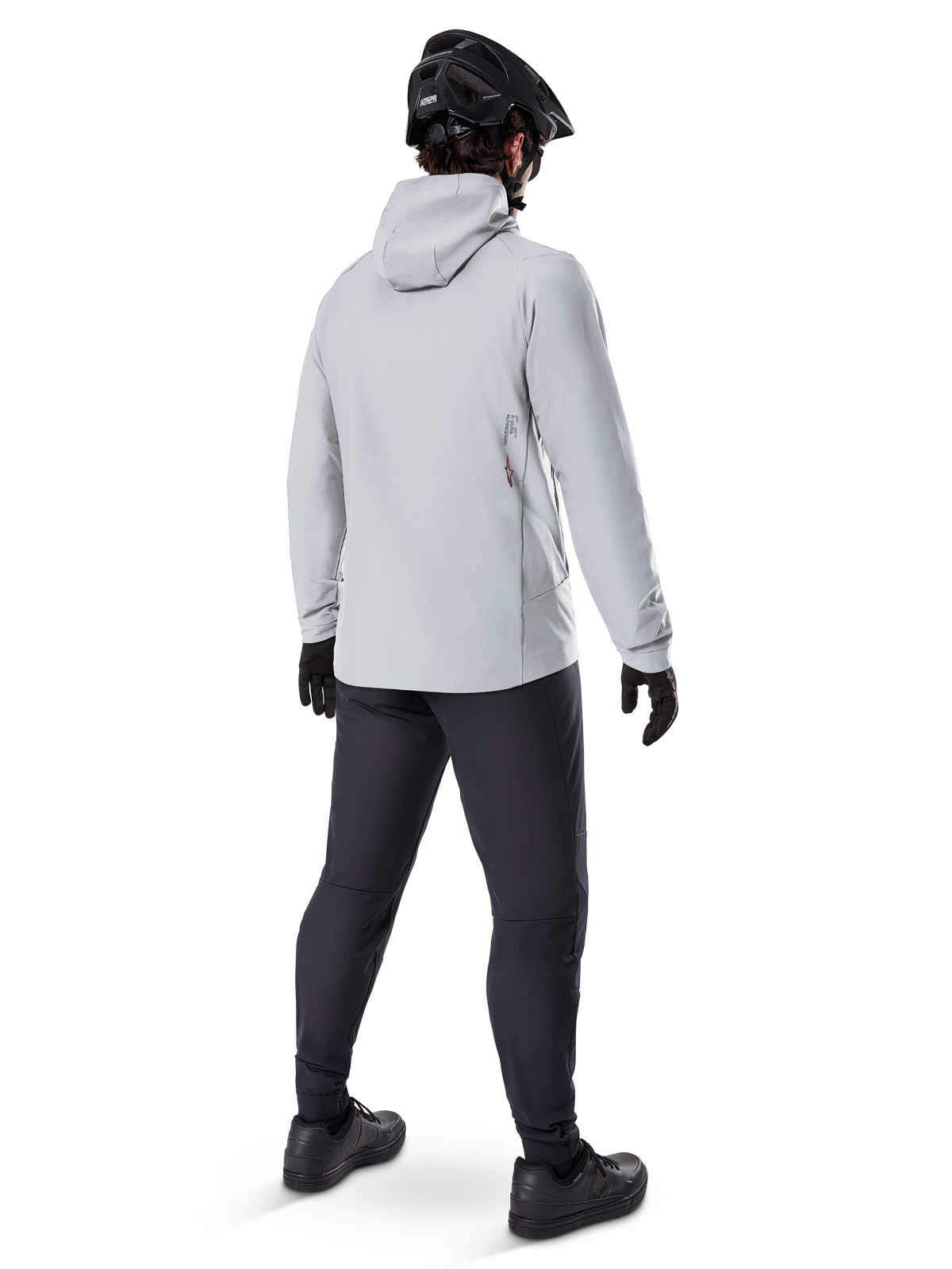 Alpinestars A-Dura Thermal Jacket i Titanium, mandlig cyklist set bagfra iført lysegrå termojakke med hætte, kombineret med sort MTB-hjelm, sorte handsker og mørkegrå bukser, funktionelt mountainbike-udstyr