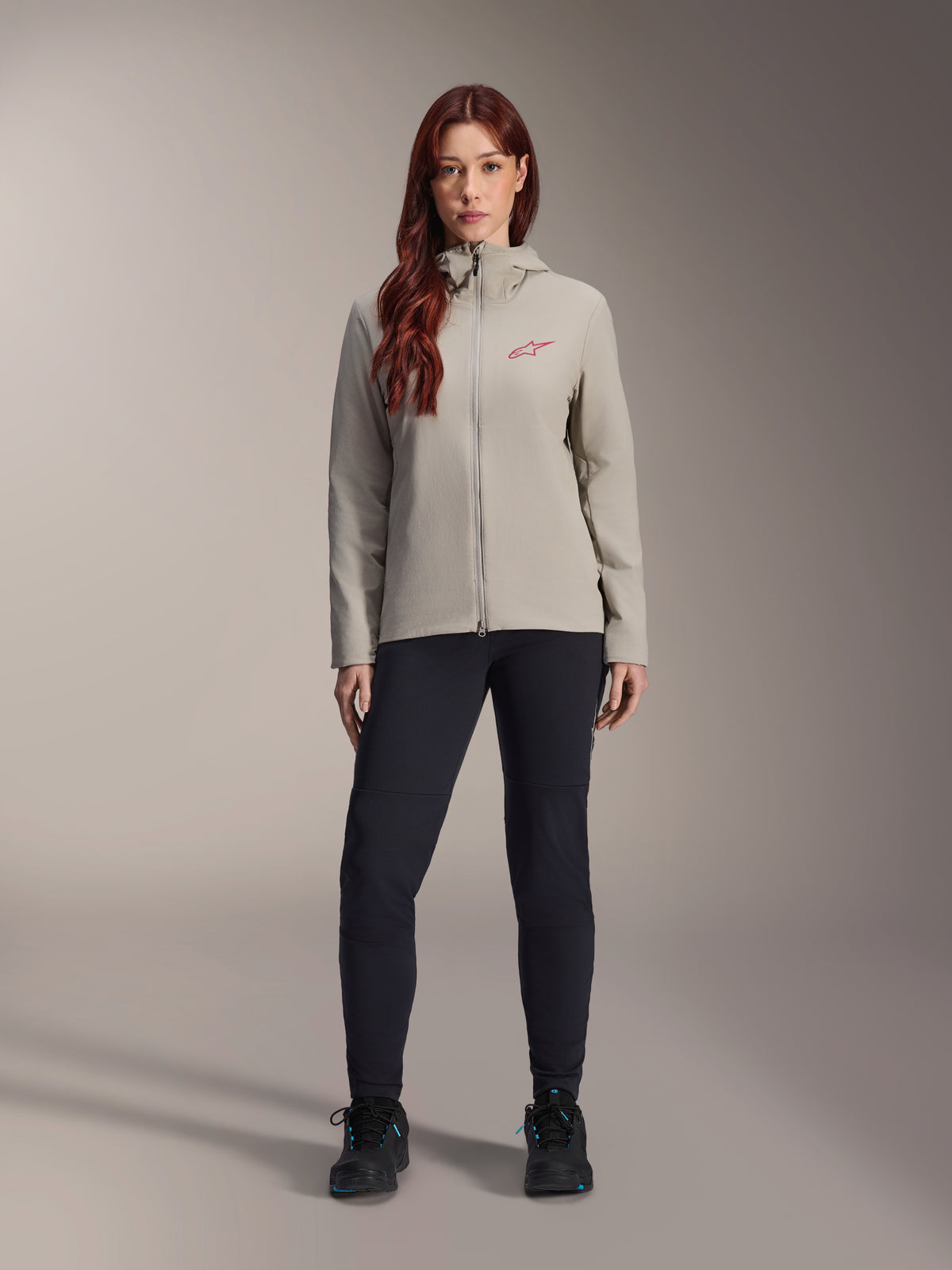 Alpinestars Stella A-Dura termojakke til kvinder, mountainbike-jakke, titaniumgrå, båret med sorte tekniske bukser og sort fodtøj, med fleece-foret hætte og rødt logo på brystet, designet til kørsel i koldt vejr