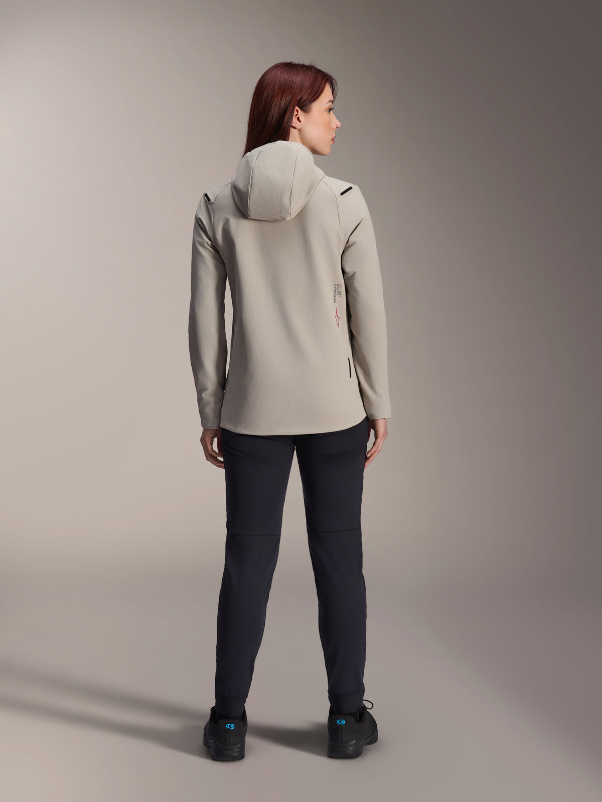 Alpinestars Stella A-Dura Thermal Jacket til kvinder, Titanium Gray, set bagfra bæres med sorte bukser, med fleece-foret isoleret hætte og et lille rødt logo, funktionel og stilfuld mountainbike-jakke til kørsel i koldt vejr.