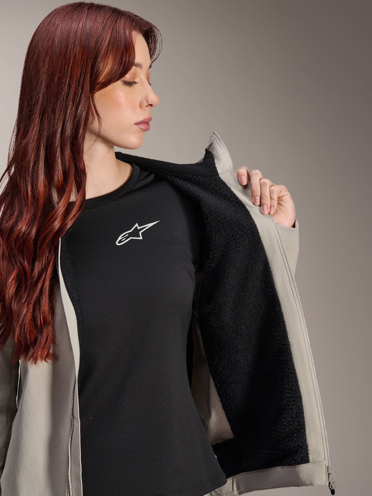 Kvinde iført Alpinestars Stella A-Dura Thermal Jacket i Titanium, som viser det sorte teksturerede fleecefor, båret over en sort t-shirt med hvidt stjernelogo, letvægts mountainbikejakke til kolde forhold