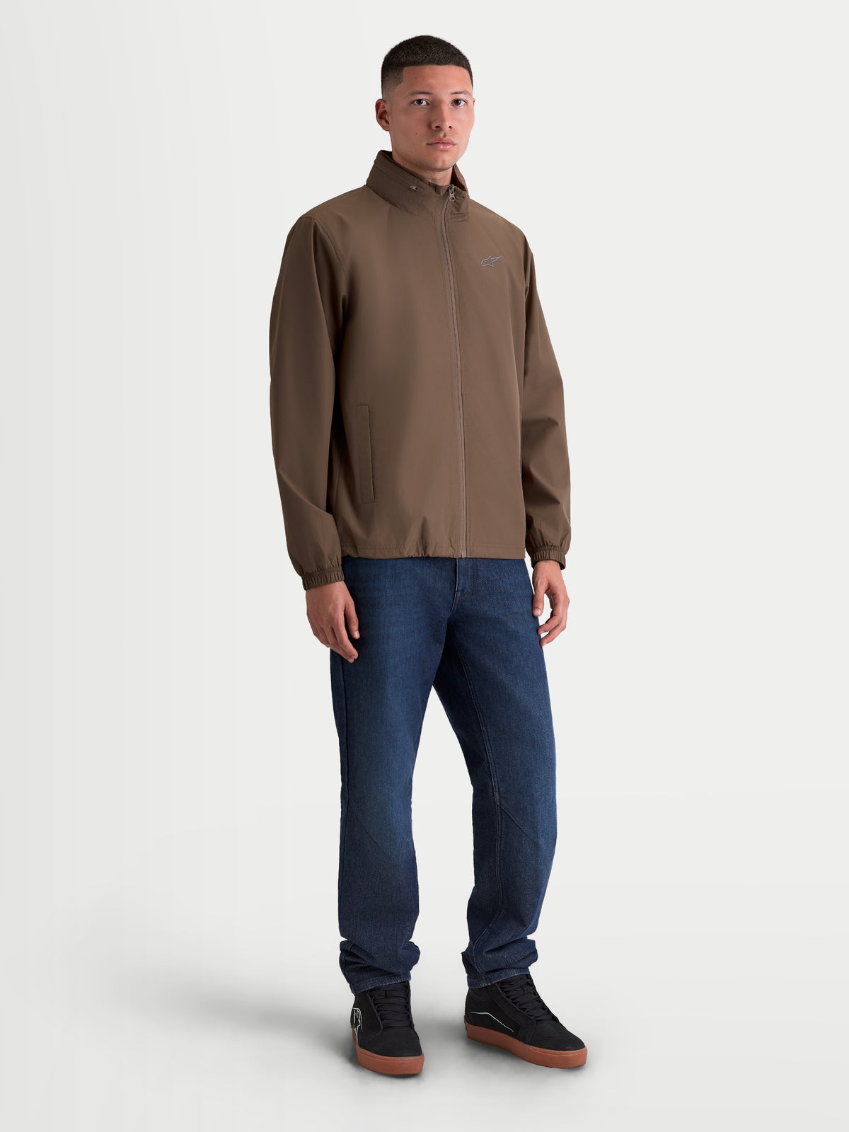 Alpinestars Overhaul Racer jakke, letvægts sportsjakke til herrer i brun, vist på model med motorsport-inspireret silhuet, pakbar skjult hætte, omvendt lynlås og diskret Astars-logo, 100 % polyester.