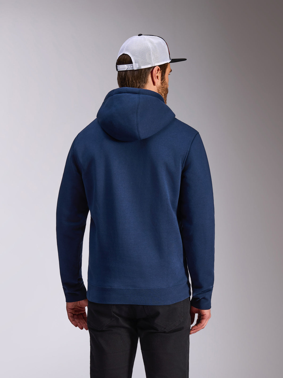 Alpinestars Frontal Hoodie, navy blue pullover fleece, back view of casual streetwear, worn with black pants and a white and black mesh cap, modern motorsport-inspired design
