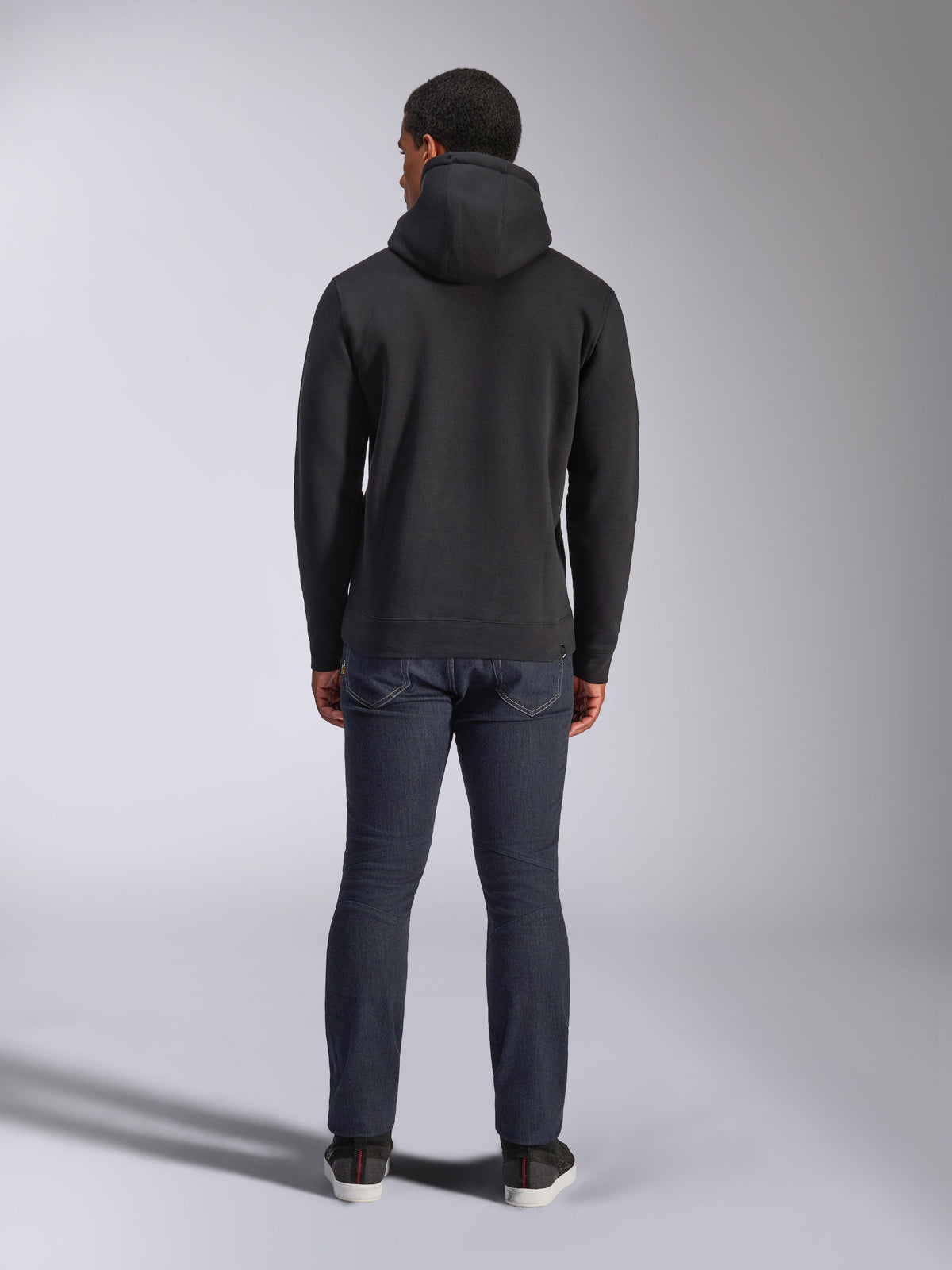 Alpinestars Blaze V3 Hoodie, casual streetwear, sort, set bagfra af hættetrøje i fleece, båret med mørkeblå denimjeans og sorte sko, rent motorsport-inspireret design