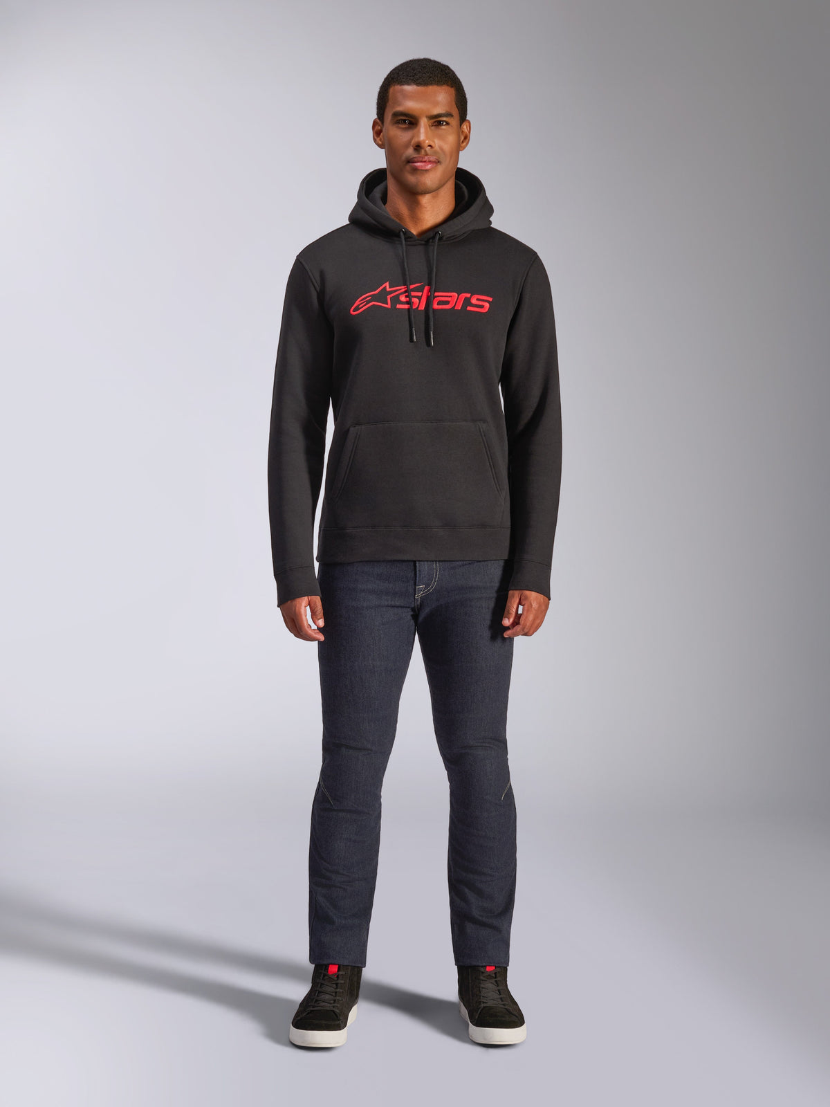 Alpinestars Blaze V3 hættetrøje, casual streetwear, sort med rødt Astars-logo, set forfra, båret af model med mørke denimbukser og sorte sneakers, moderne motorsport-inspireret fleecedesign