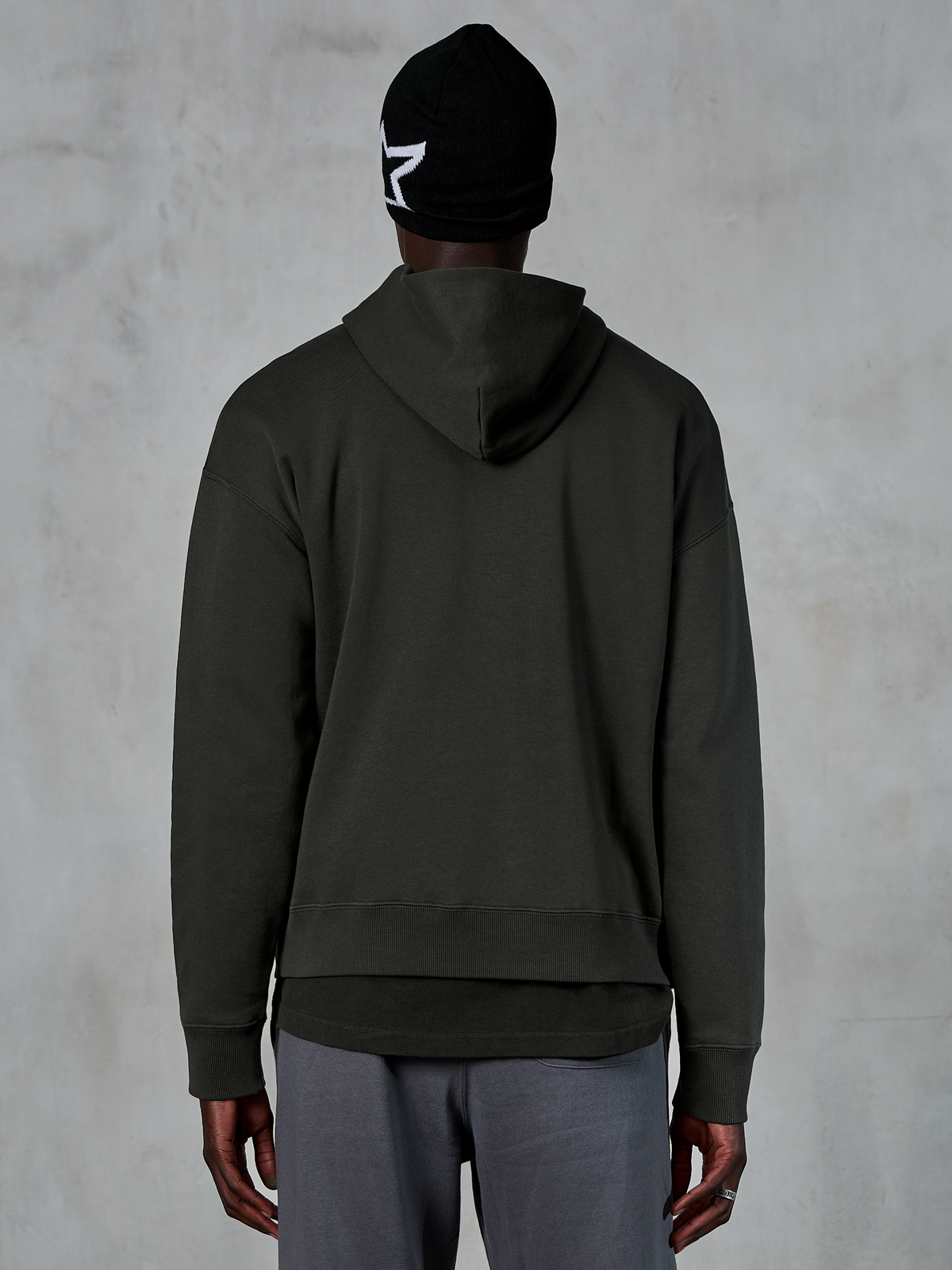 Alpinestars Essentials Ageless Hoodie, set bagfra, Off Black, afslappet streetwear, model iført sort beanie med hvidt stjernelogo og grå bukser, premium fleece med stenvasket finish