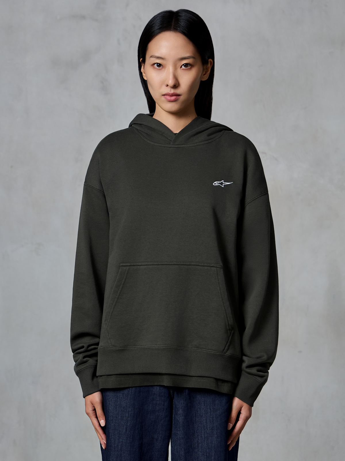 Alpinestars Essentials Ageless Hættetrøje, Off Black, båret af en model, med et lille hvidt Astars-logo på brystet, kængurulomme foran, stenvasket finish, afslappet premium fleece streetwear
