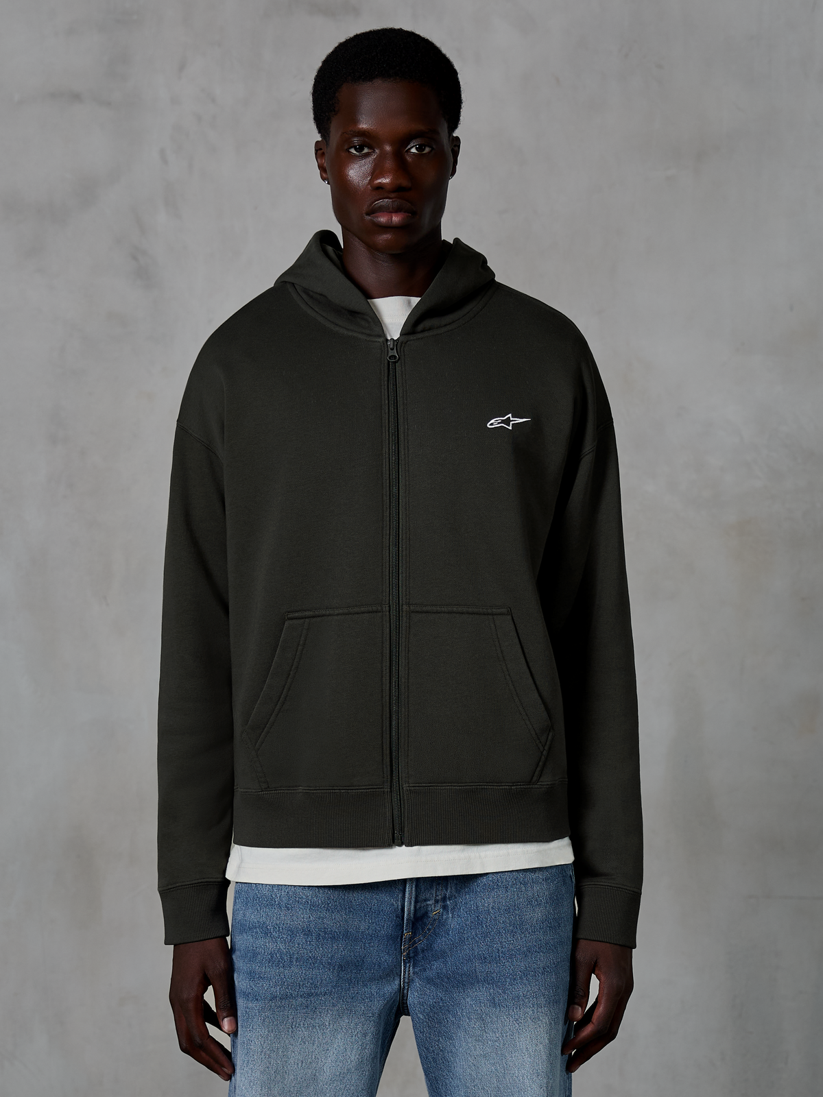 Alpinestars Essentials Ageless Zip Hoodie, hættetrøje med lynlås, Off Black, med et lille hvidt stjernelogo på brystet, lommer foran og ribstrikkede manchetter, båret som afslappet motorsport-inspireret streetwear
