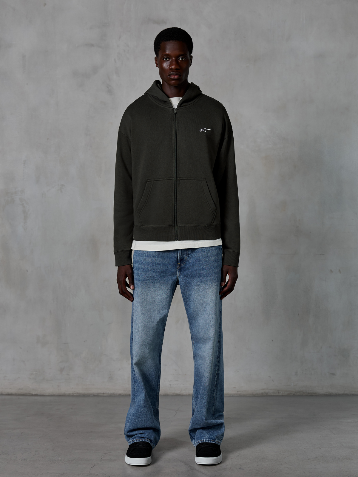 Alpinestars Essentials Ageless Zip Hoodie, hættetrøje med lynlås, Off Black, med et lille hvidt Alpinestars-logo på brystet, båret af en model med hvid t-shirt og blå jeans, afslappet pasform, casual motorsport streetwear