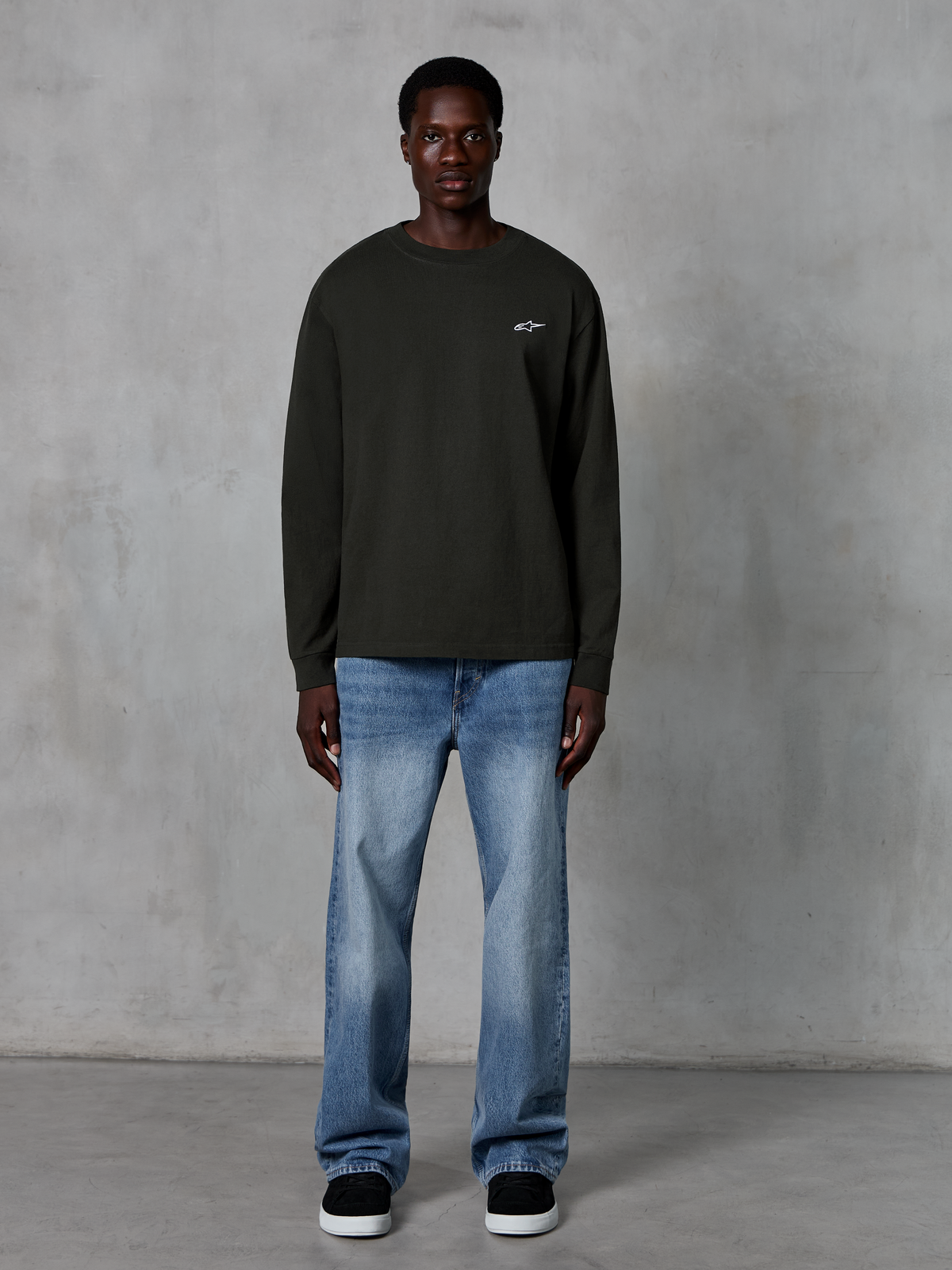 Alpinestars Essentials Ageless LS Tee, langærmet t-shirt, Off Black, med et lille hvidt stjernelogo på brystet, afslappet pasform, casual motorsport-streetwear, stylet med lyseblå jeans