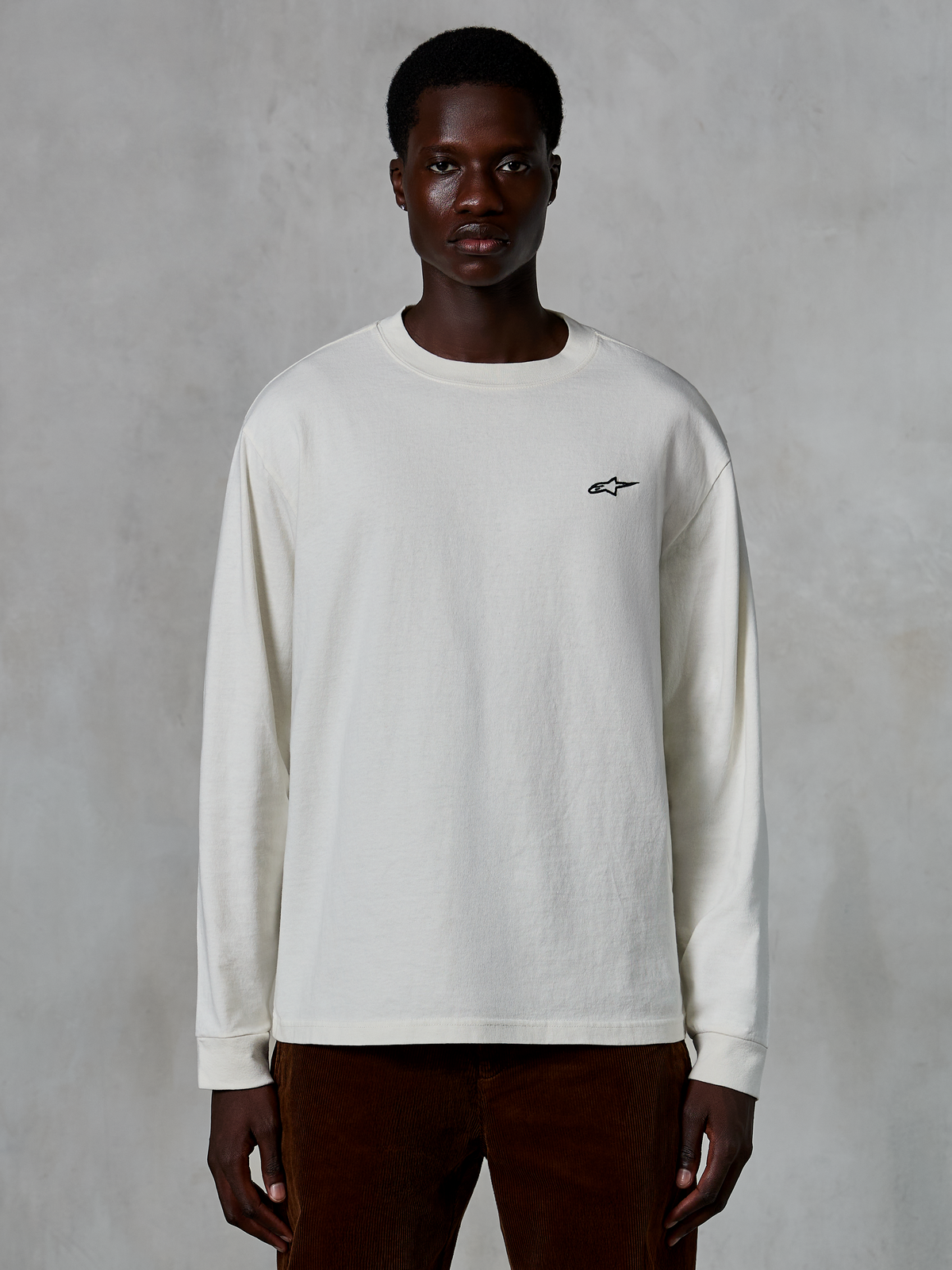 Alpinestars Essentials Ageless LS Tee, langærmet T-shirt, råhvid, lille sort stjernelogo på brystet, afslappet streetwear, afslappet pasform, båret af en model
