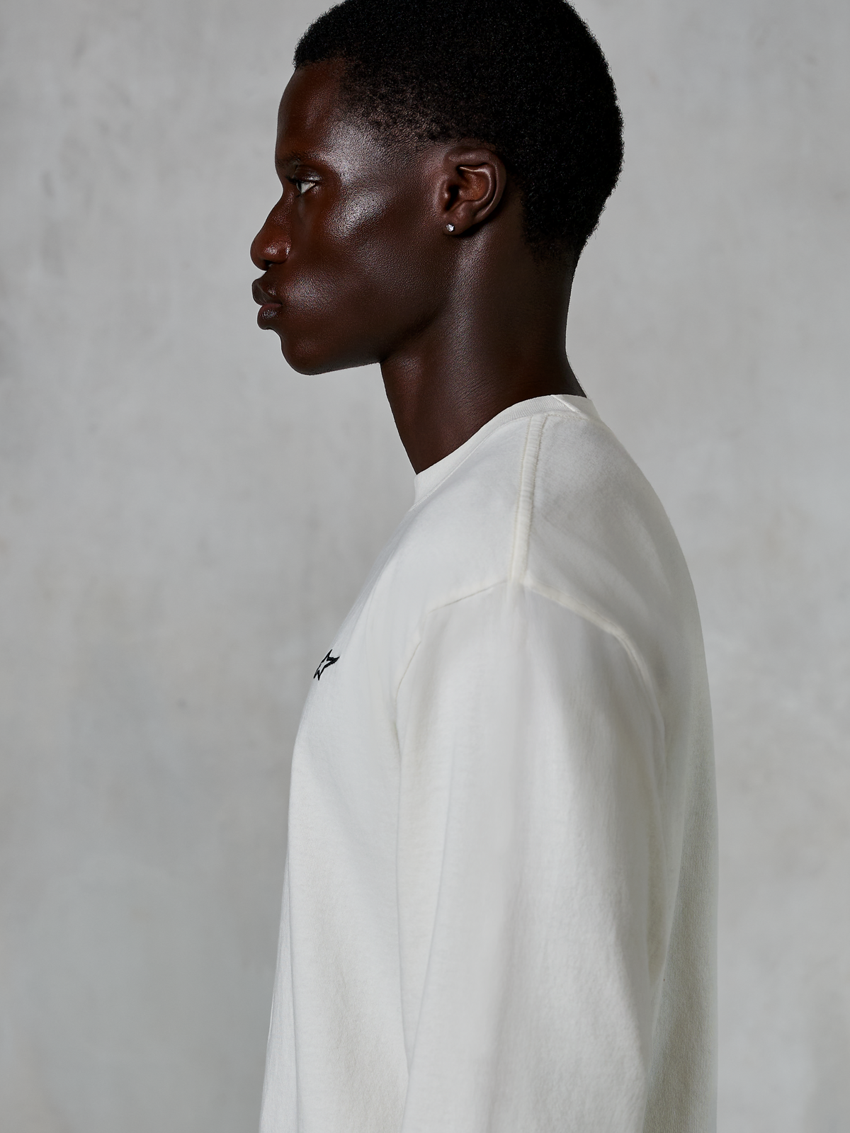 Alpinestars Essentials Ageless LS Tee, langærmet t-shirt, råhvid, profilvisning af en mand iført t-shirt med afslappet pasform, lille sort logo på brystet, afslappet motorsport-inspireret livsstilstøj