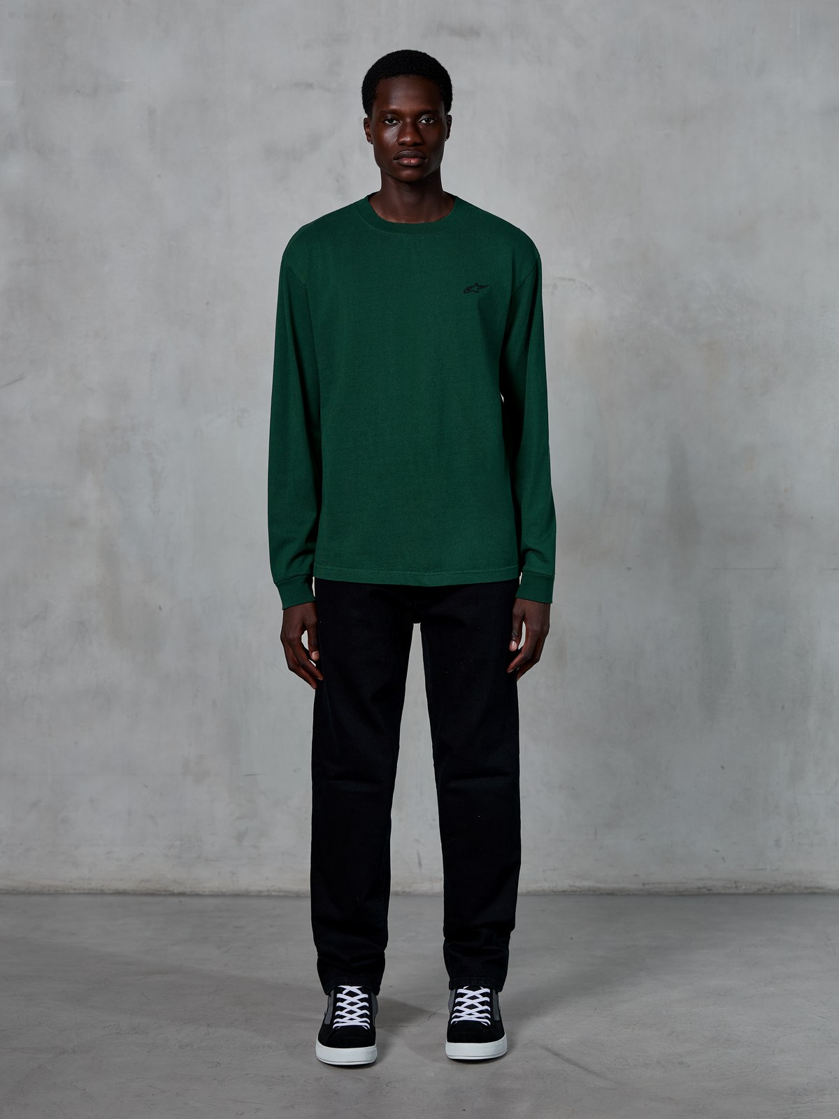 Alpinestars Essentials Ageless LS Tee, langærmet T-shirt, Pine Green, med et lille sort logo på brystet, båret af en model med sorte bukser og sneakers, afslappet streetwear-stil