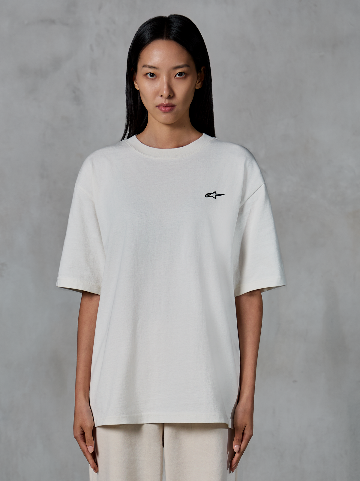 Alpinestars Essentials Ageless SS Tee, kortærmet T-shirt, off-white, båret af kvindelig model, med et lille sort Alpinestars-logo på brystet, afslappet pasform, afslappet lifestyle streetwear