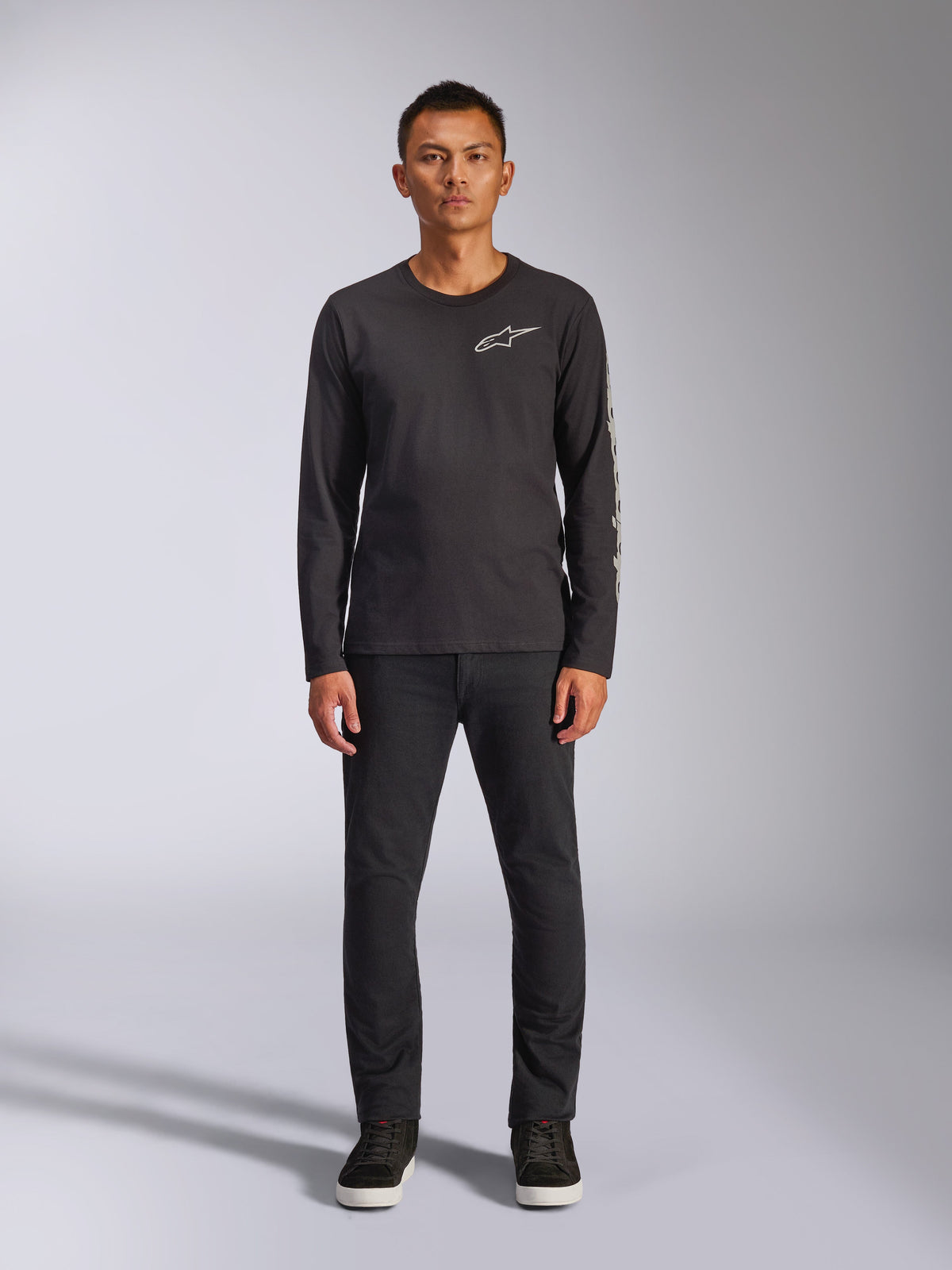 Alpinestars Trackside CSF Tee, langærmet t-shirt, sort, hvidt Alpinestars-logo på brystet og grafisk branding på ærmet, båret med sorte bukser og sneakers, afslappet motorsport-inspireret streetwear