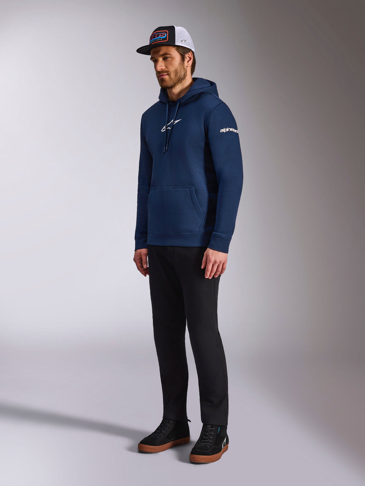 Alpinestars Frontal Hoodie in Navy Blue, casual fleece pullover featuring white Astars logo on the chest and wordmark on the sleeve, styled with a trucker hat and black pants, modern motorsport-inspired lifestyle apparel.