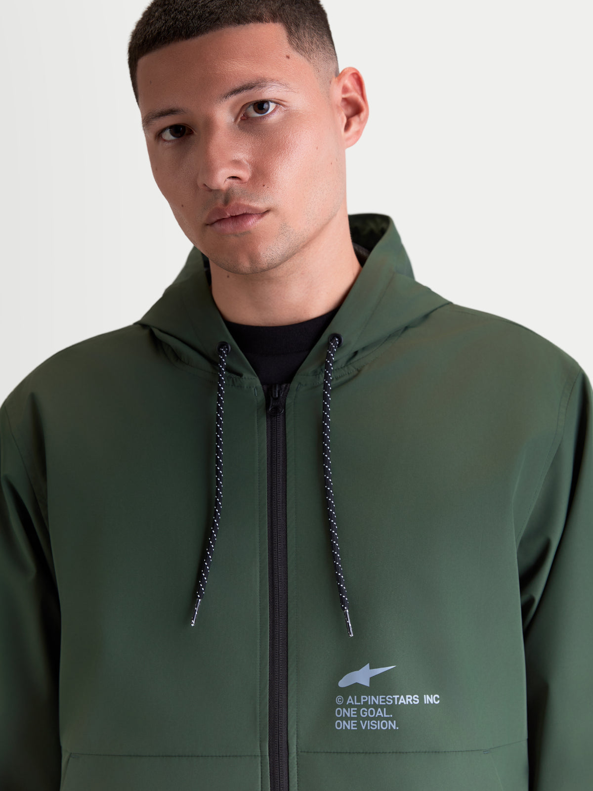 Alpinestars Speeder Resolve windbreaker-jakke, letvægts sportswear-windbreaker i grøn med justerbar hætte, spættede snoretræk og signatur Alpinestars-branding på brystet, båret af en herremodel.