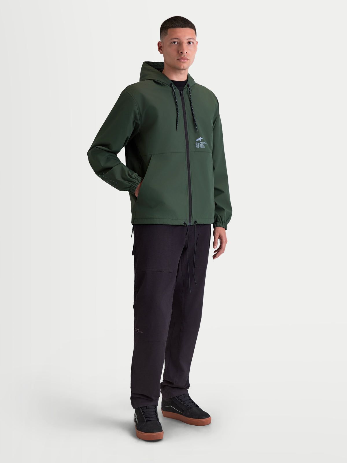 Alpinestars Speeder Resolve Windbreaker Jakke, letvægts sportswear-windbreaker til herrer, grøn, polyesterkonstruktion med mesh-for, justerbar hætte og Alpinestars-logo på brystet, vist på model til urban brug.