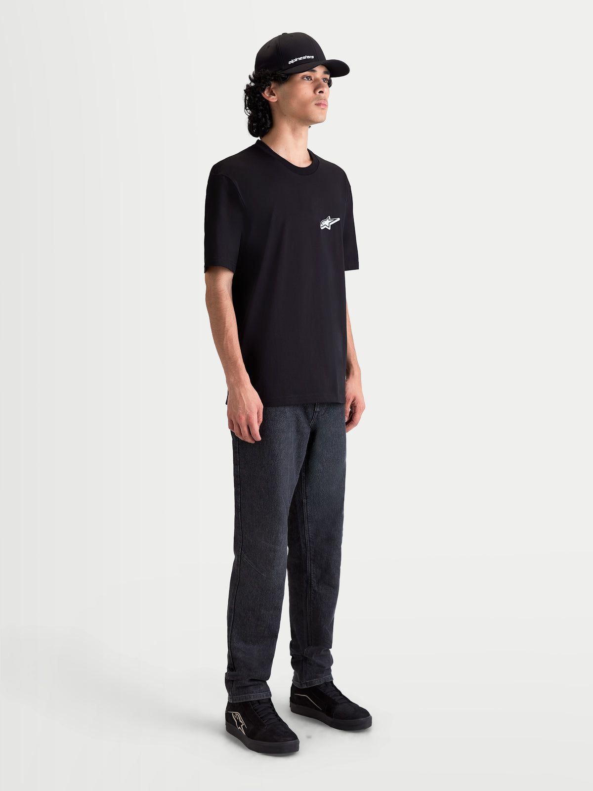 Alpinestars Meteor CSF t-shirt, herre-t-shirt med korte ærmer, sort med hvidt MX-inspireret logo på brystet, afslappet lifestyle og motorsport sportstøj, model iført sort t-shirt og mørke jeans