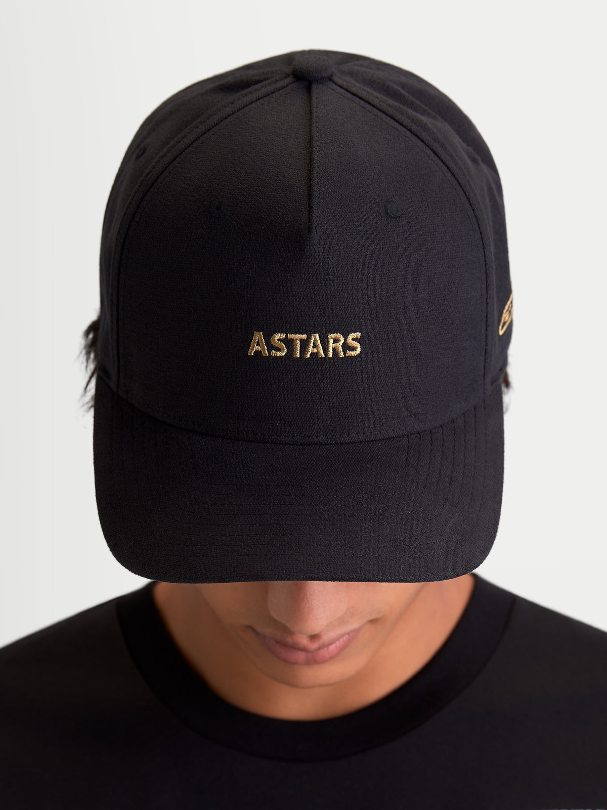Alpinestars County Canvas Kasket, sort sportswear-kasket med guld ASTARS-logobroderi, buet skygge og struktureret krone, motorsport-inspireret kasket til hverdagsbrug i peached oxford-stof, set forfra på model