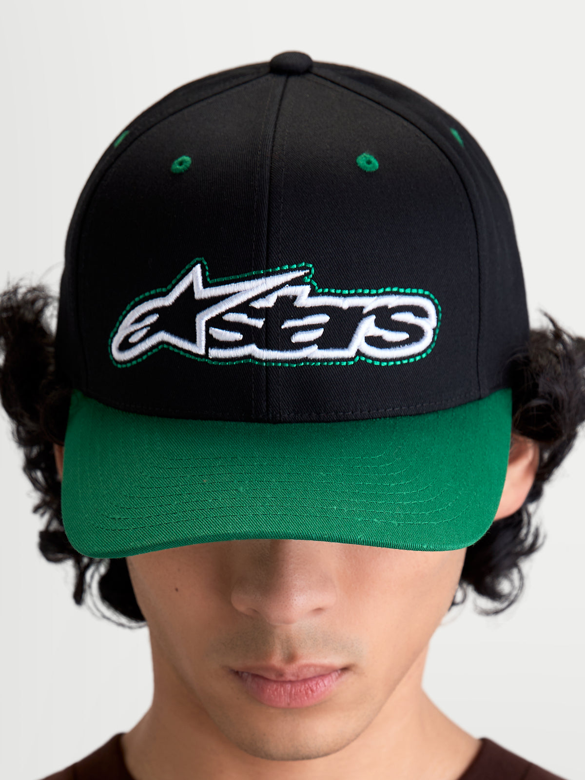 Alpinestars Retro Snapback kasket, motorsportsinspireret baseballkasket med buet skygge og struktureret krone, unisex, sort og grøn, bomuldstwill, set forfra på model med broderet Astars-logo og grønne detaljer.