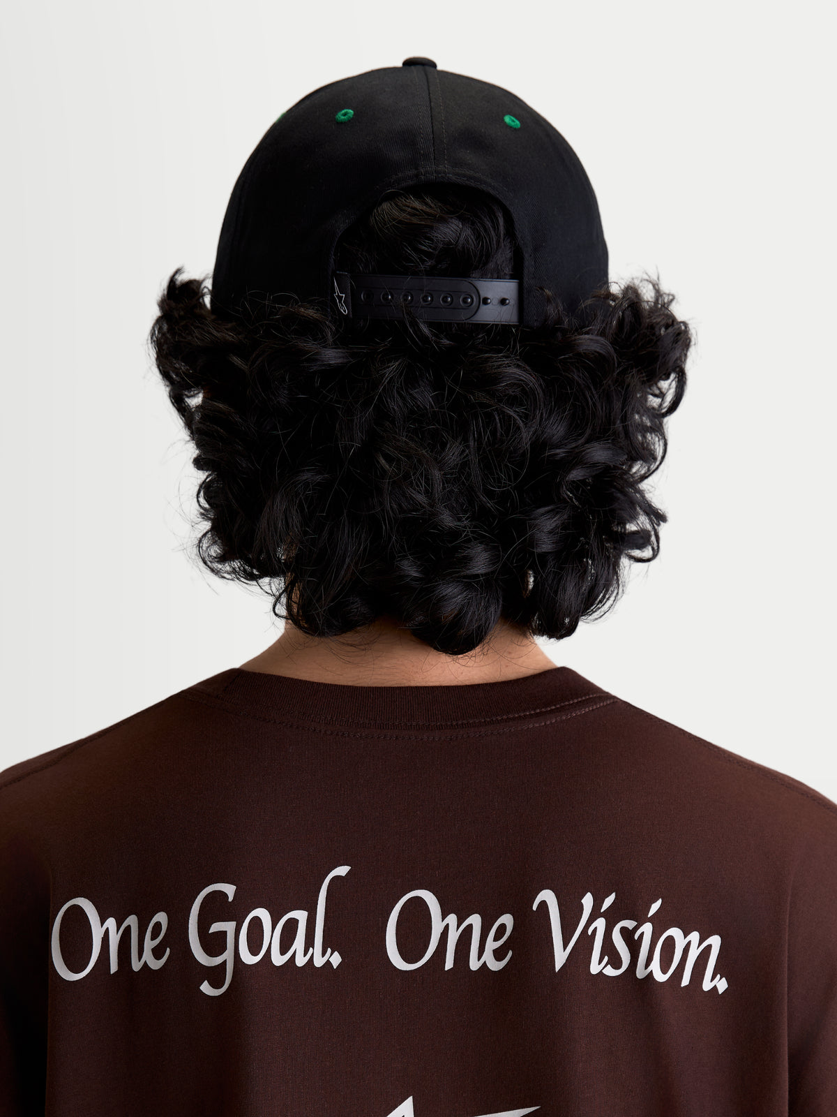 Alpinestars Retro Snapback Kasket, sportswear snapback-kasket, sort og grøn, set bagfra på model med justerbar snapback-lukning og grønne lufthuller, båret med en brun t-shirt med Alpinestars One Goal. One Vision. brand-manifesto.