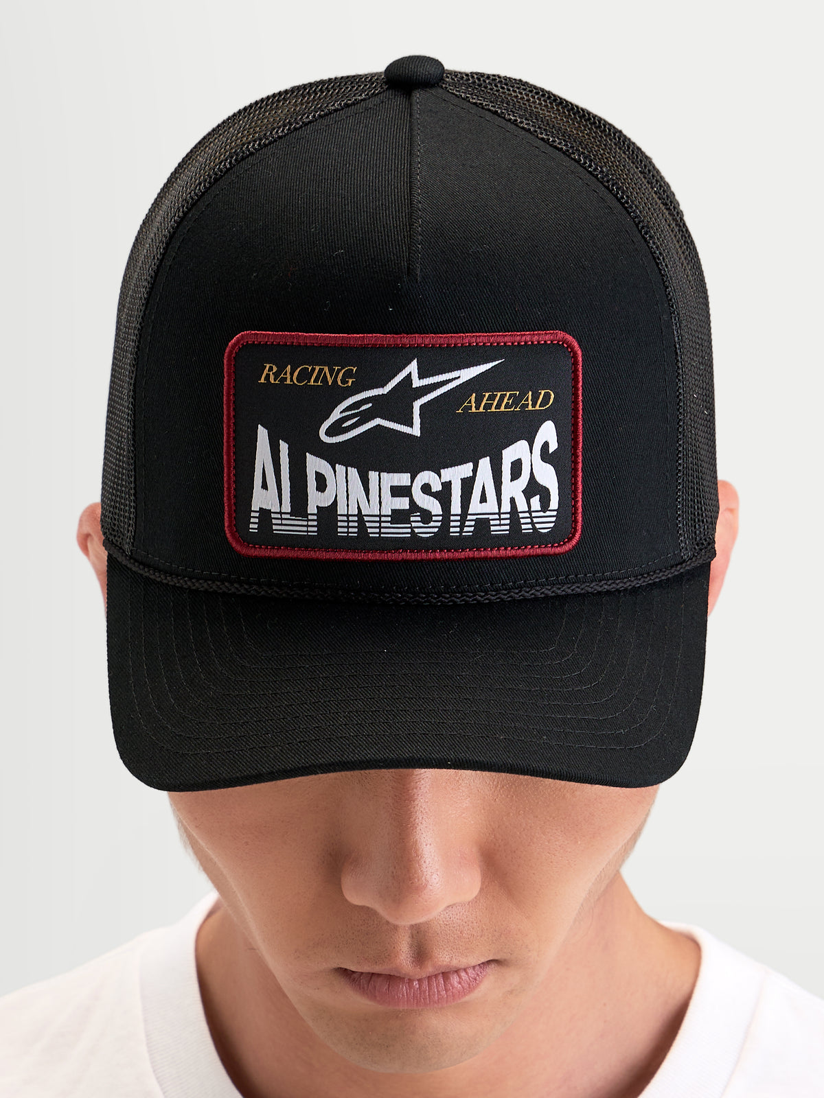 Alpinestars Hemmings Trucker Cap, sort kasket med vævet logomærke foran og åndbare mesh-bagpaneler, båret af model