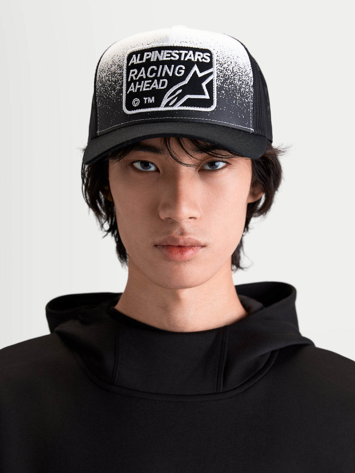 Alpinestars Gravel Trucker cap, livsstilskasket til sportstøj, sort og hvid, set forfra på model med buet skygge, åndbar mesh-bagside og vævet Racing Ahead-patch med grusstruktur-detaljer.