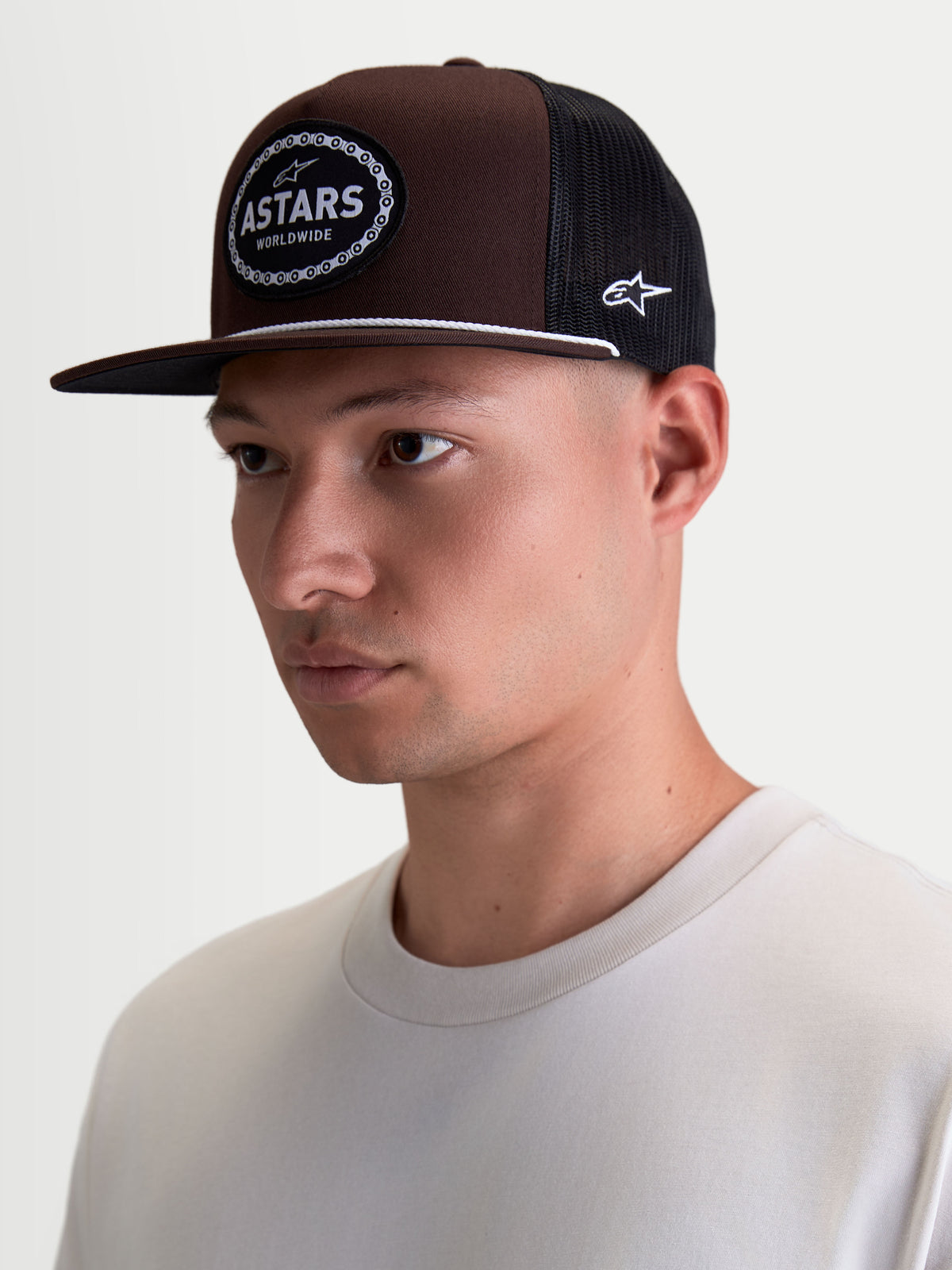 Alpinestars Hotlink Trucker kasket på model, brun og sort motorsport-inspireret kasket med flad skygge, struktureret twill-krone og vævet Astars-logomærke med cykelkædekant, casual streetwear