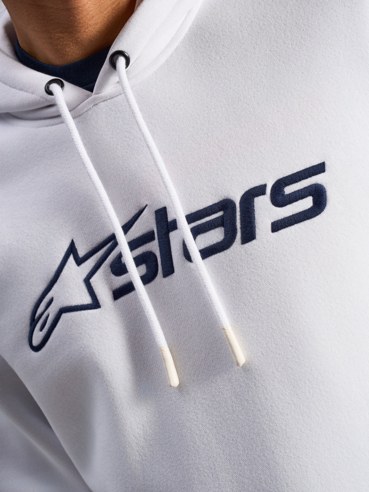 Alpinestars Blaze V3 hættetrøje, hvid og navyblå, nærbillede af brystet med navyblåt logoprint på fronten og hvide snore med dyppede spidser, afslappet motorsport-streetwear