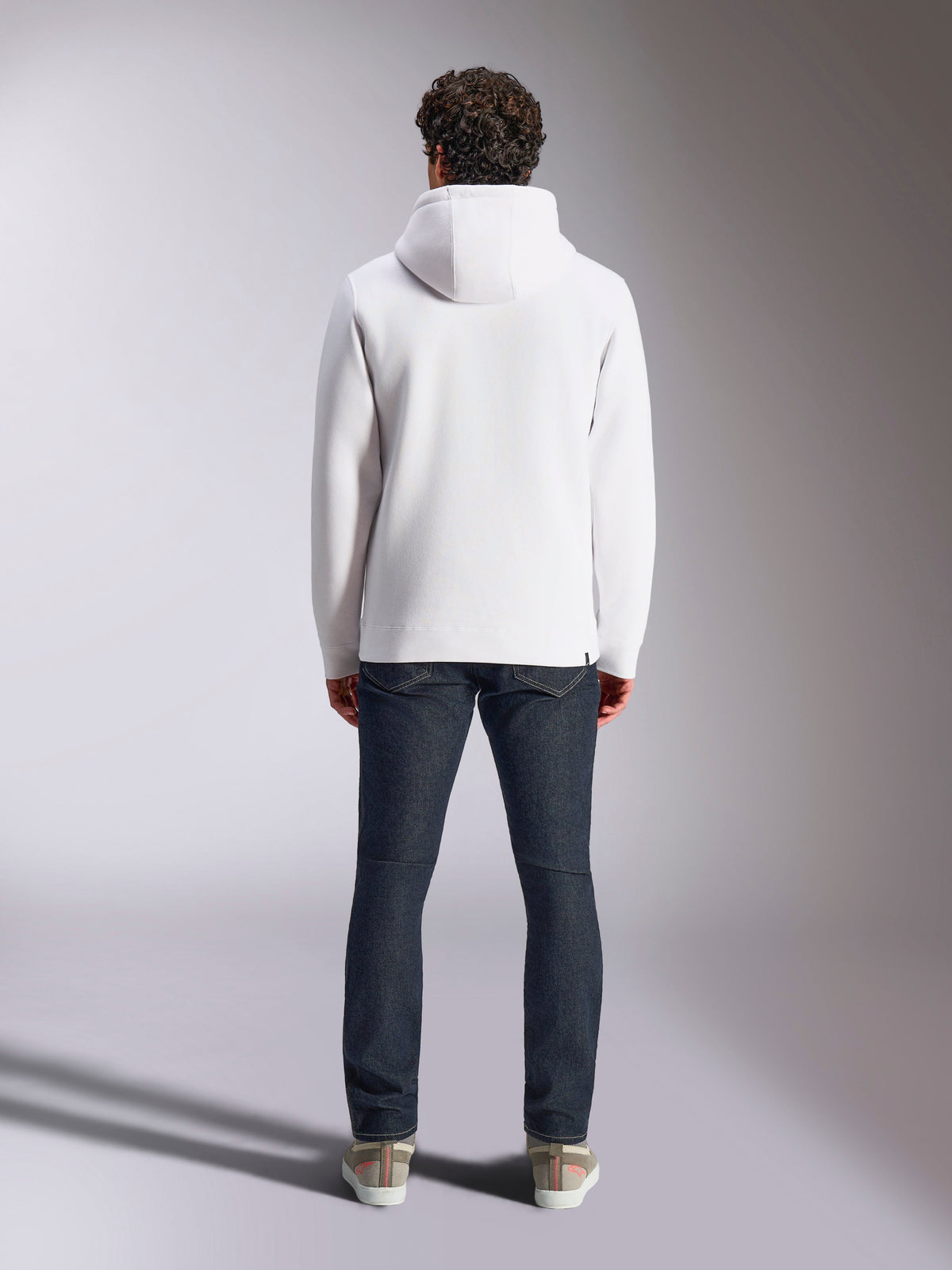 Alpinestars Blaze V3 hættetrøje, hvid afslappet sportstøjs-hættetrøje, set bagfra, pullover i fleece, stilrent design med ribkanter ved manchetter og søm, stylet med mørkeblå jeans og sneakers, moderne motorsport-inspireret livsstilstøj