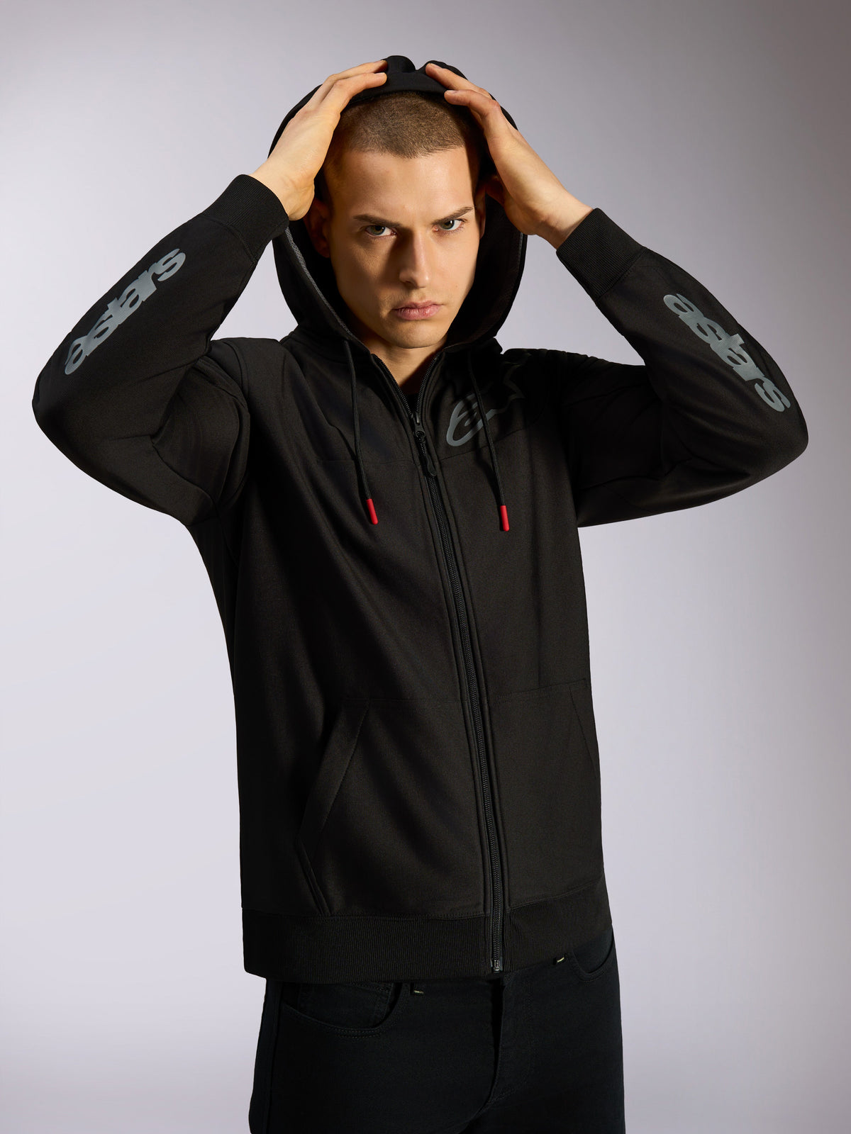 Alpinestars Sessions V3 Hoodie, black full-zip hoodie, grey Astars branding on forearms, mesh-lined hood with red-tipped drawcords, casual motorsport-inspired streetwear