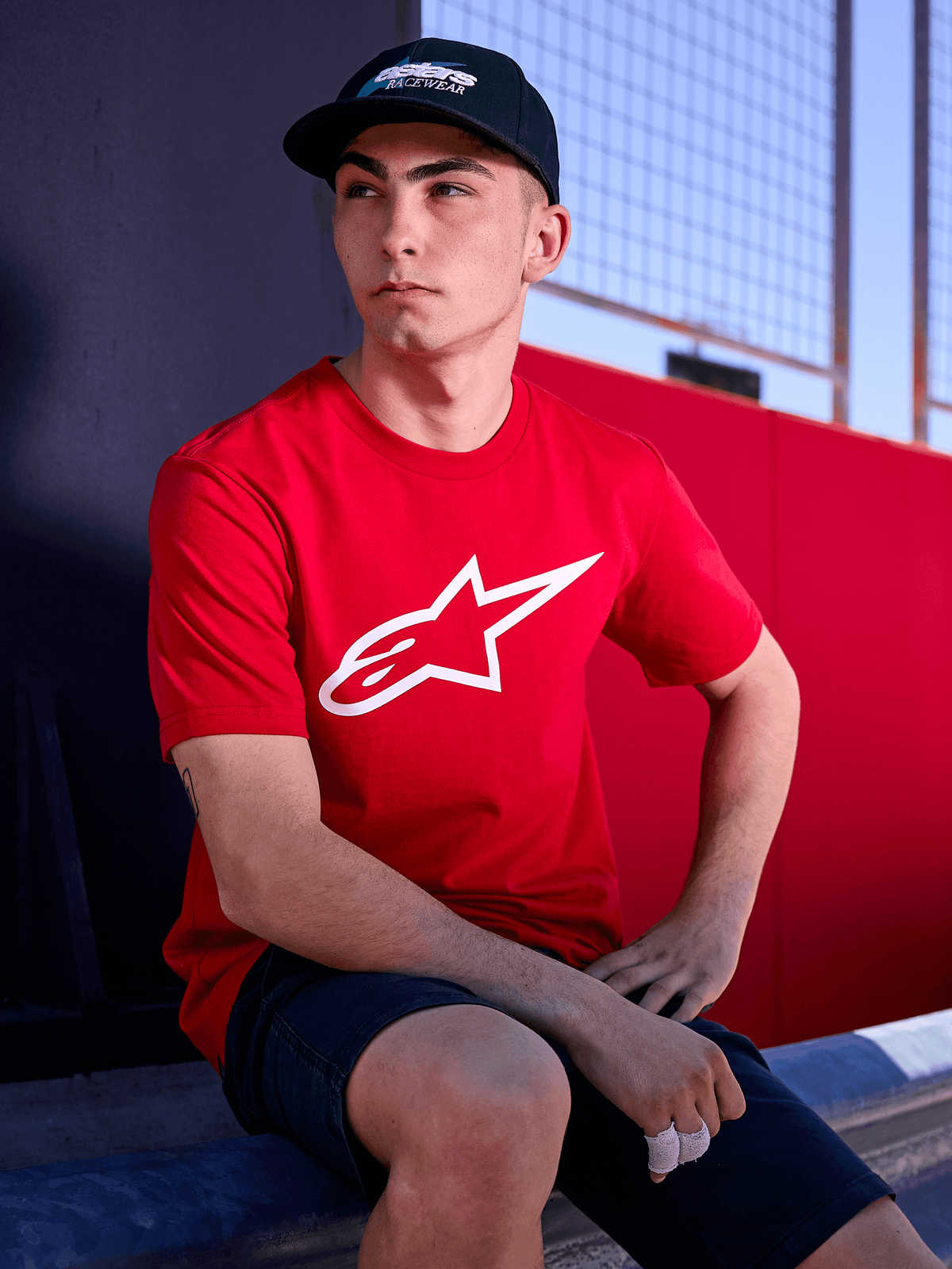 Alpinestars Profile kasket i sort, lifestyle-billede af en mand iført kasketten med buet skygge og en rød t-shirt med hvidt Alpinestars-logo, afslappet motorsport-inspireret streetwear