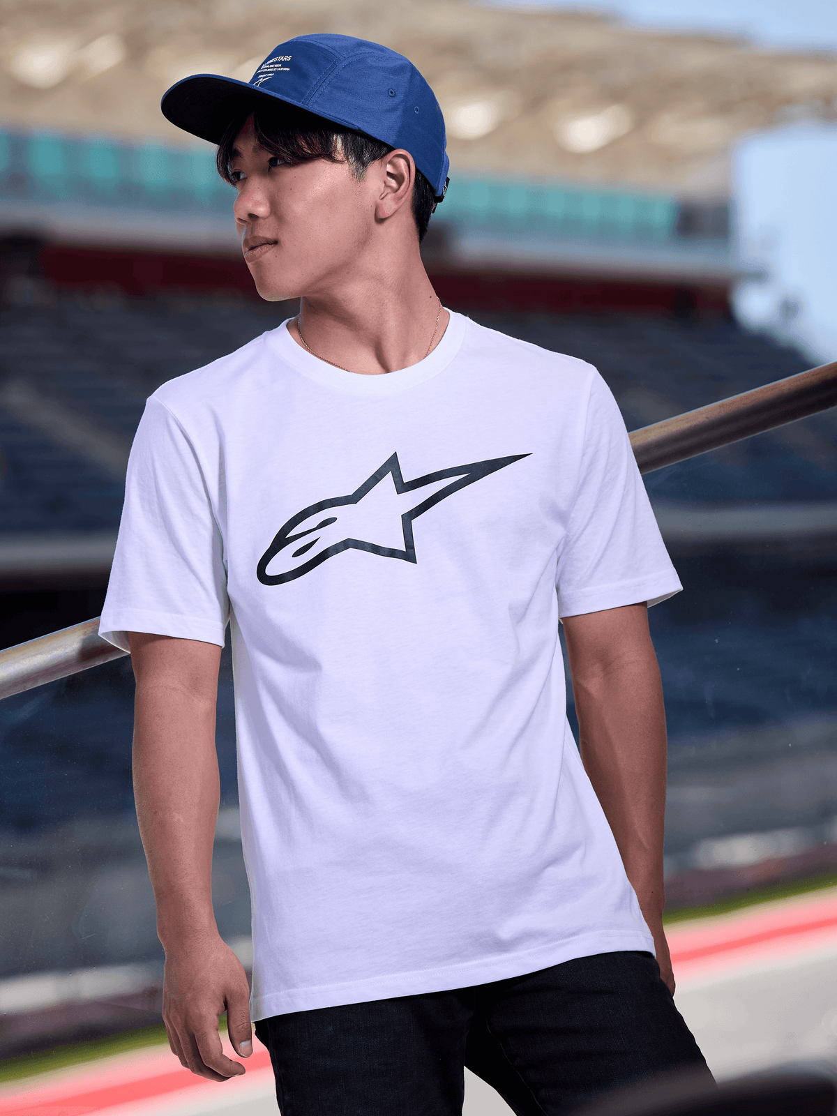 Man wearing Alpinestars Peasy Hat in Blue, 5-panel jockey hat with flat bill and white graphic logo print, styled with a white Alpinestars logo T-shirt, casual motorsport-inspired streetwear