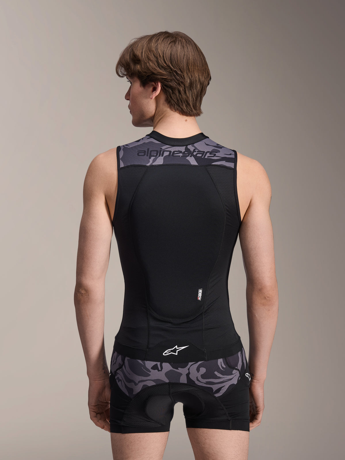 Alpinestars A-Motion Plasma beskyttelsesvest, Black Camo, set bagfra på mandlig model, åndbar mesh-konstruktion med integreret Nucleon Plasma rygbeskytter, grå camouflage-detaljer på skuldre og talje, Alpinestars-branding