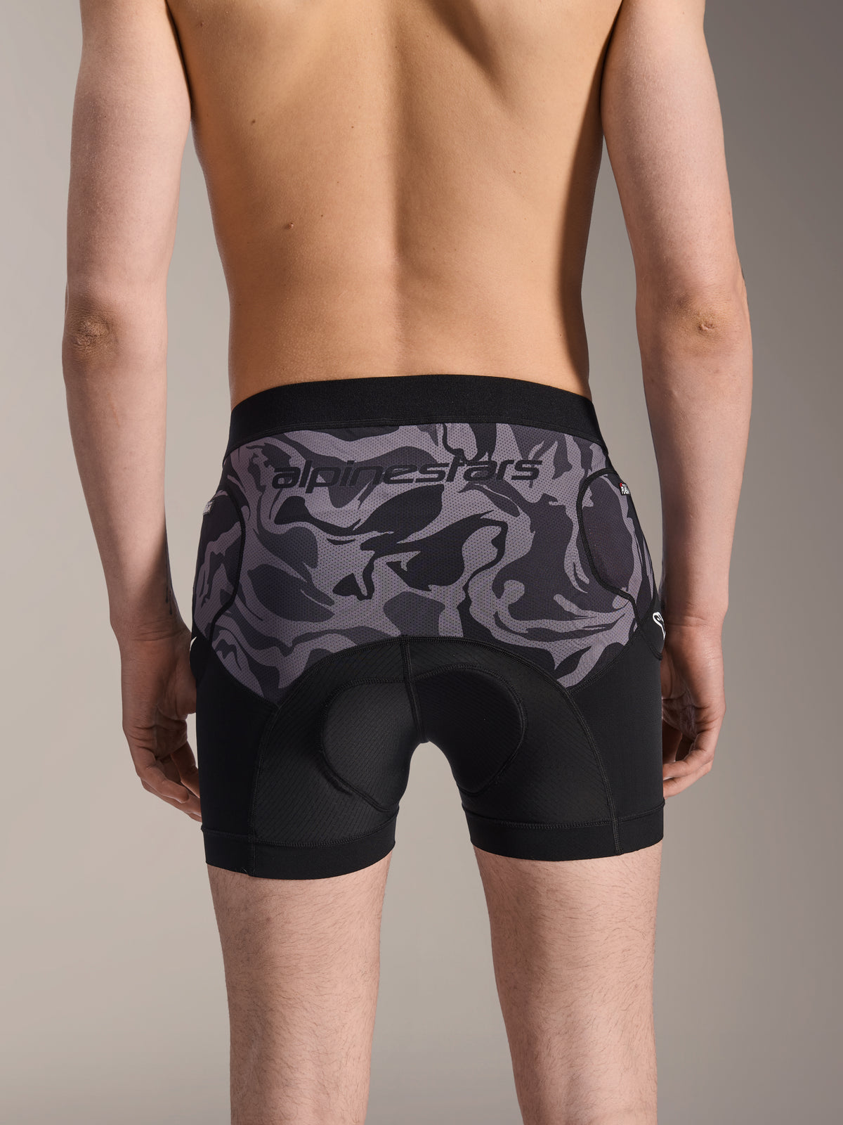 Alpinestars A-Motion Plasma beskyttelsesboxershorts, MTB beskyttelsesshorts, Black Camo, set bagfra på en model, med Alpinestars-logo på et camo-mesh-panel, integreret chamois-pude og lommer til hoftebeskyttelse, åndbart baselag til off-road cykling