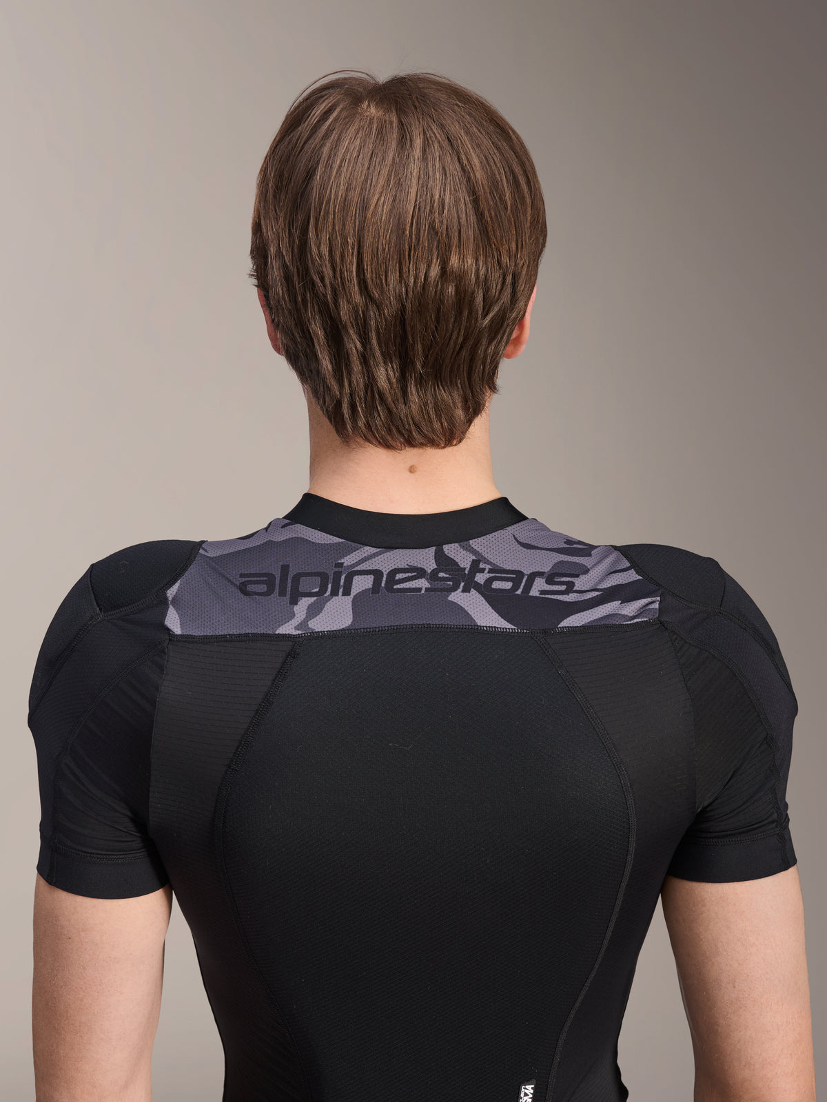Alpinestars A-Motion Plasma beskyttelsesjakke - kortærmet, set bagfra af den øvre torso, sort med gråt camo-panel over skuldrene med Alpinestars-logo, åndbar strækbar mesh-konstruktion til MTB-beskyttelse