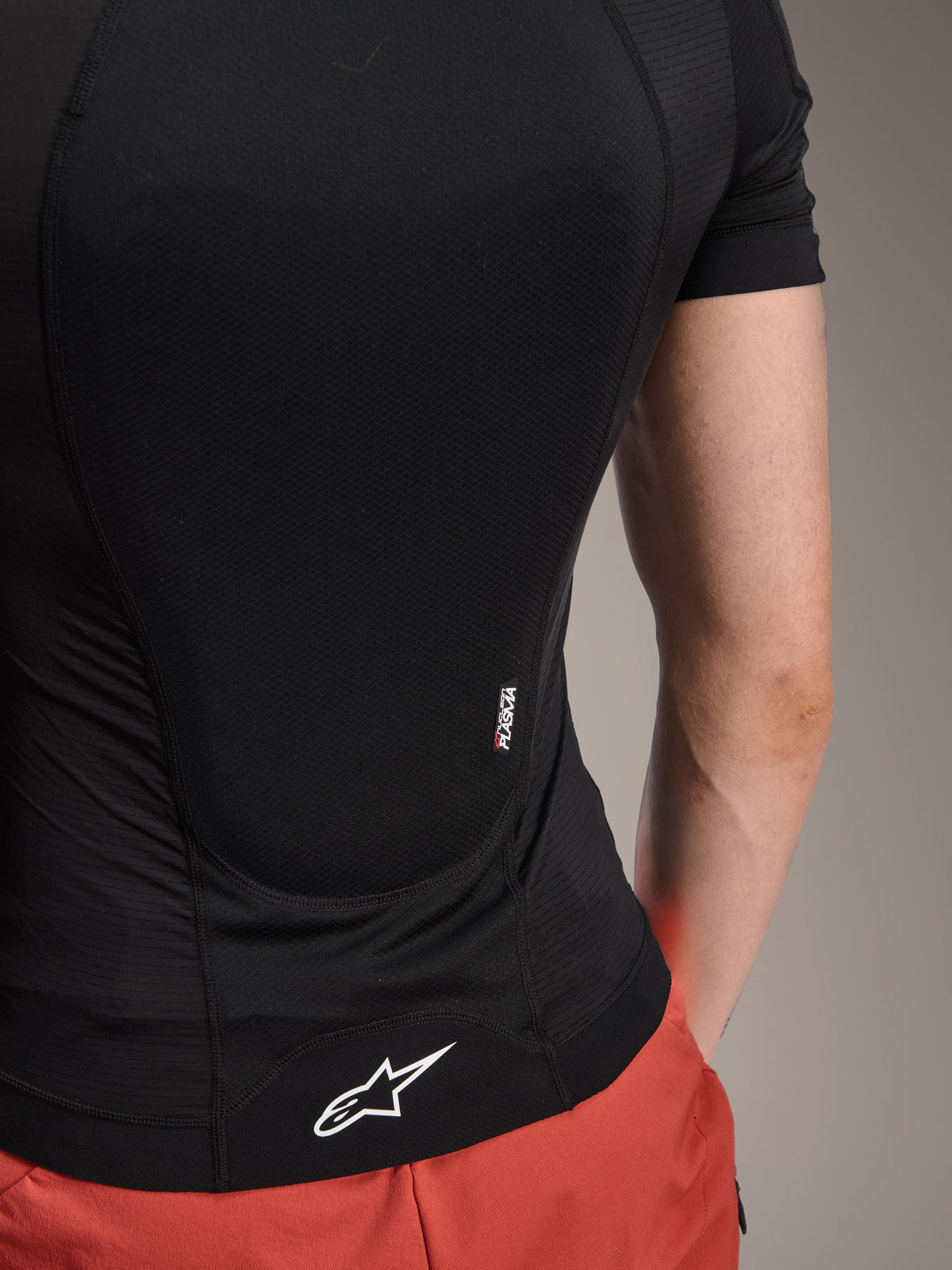 Alpinestars A-Motion Plasma beskyttelsesjakke - kortærmet, Black Camo, detalje set bagfra med Nucleon PLASMA-branding og hvidt Alpinestars-logo på kanten, åndbar strækmesh-konstruktion til MTB-beskyttelse