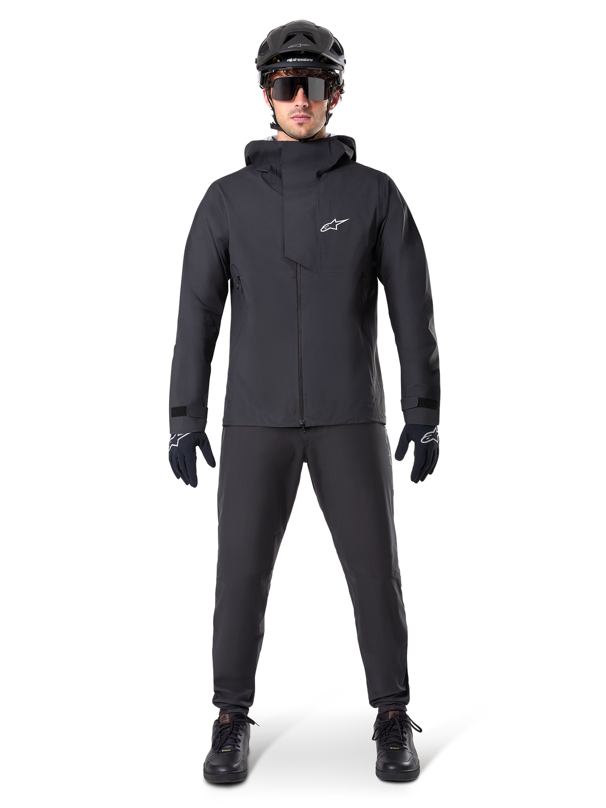 Alpinestars A-Dura Waterproof Pants, sorte MTB-bukser, båret som en del af et komplet helt sort mountainbike-udstyrssæt inklusiv en teknisk vandtæt jakke, sort hjelm, solbriller og handsker, designet til terrænkørsel i vådt vejr.