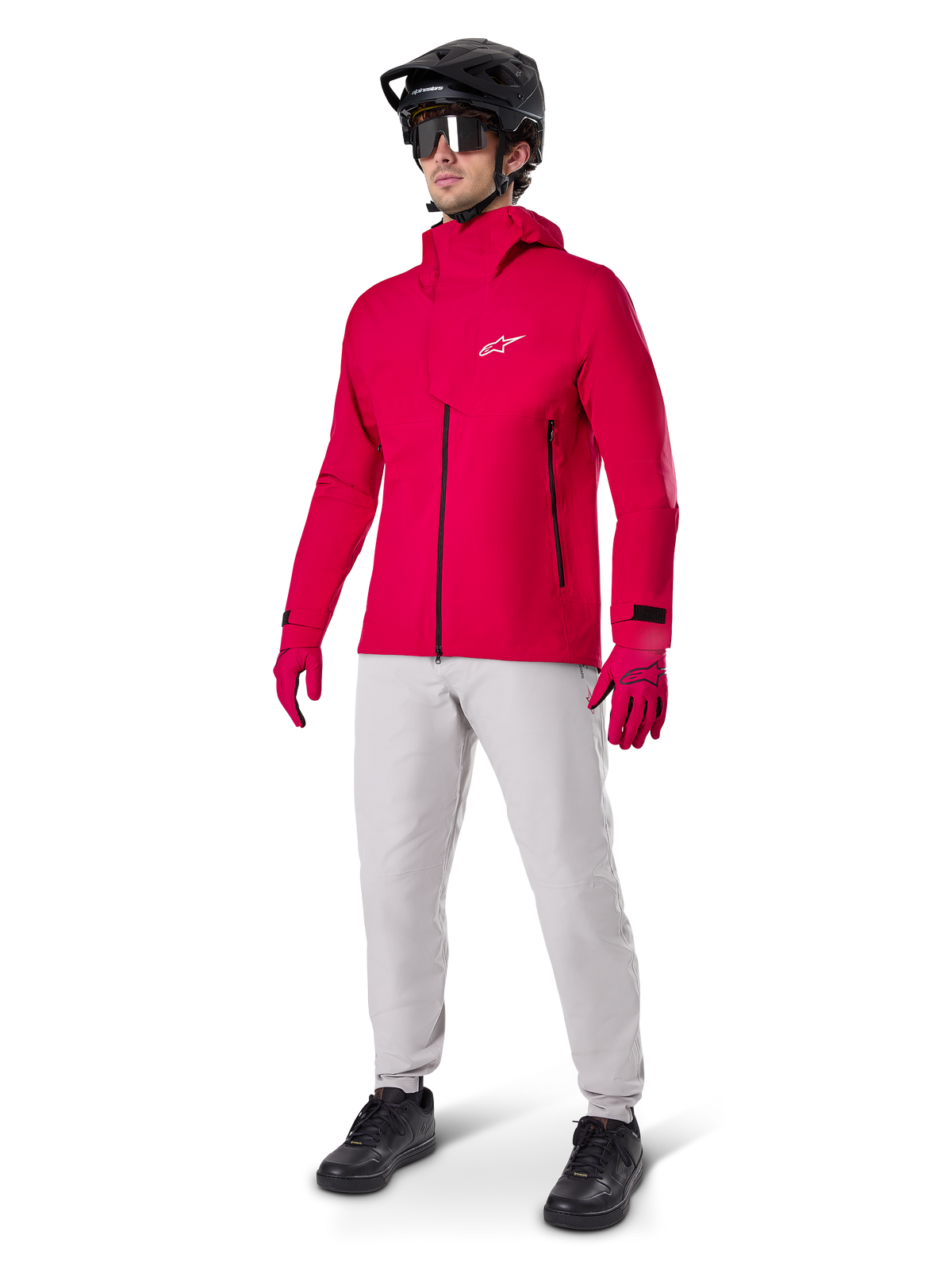 Model iført Alpinestars A-Dura vandtætte bukser i Titanium-grå, kombineret med en klar rød vandtæt jakke og matchende handsker, sort mountainbikehjelm med goggles og sorte sko, komplet mountainbike-udstyr til våde sporforhold