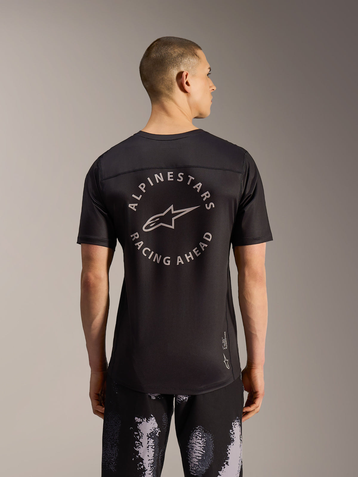 Alpinestars A-Dura Ride shorts i Black Camo og sort MTB-jersey med ryglogo, set bagfra på en model.