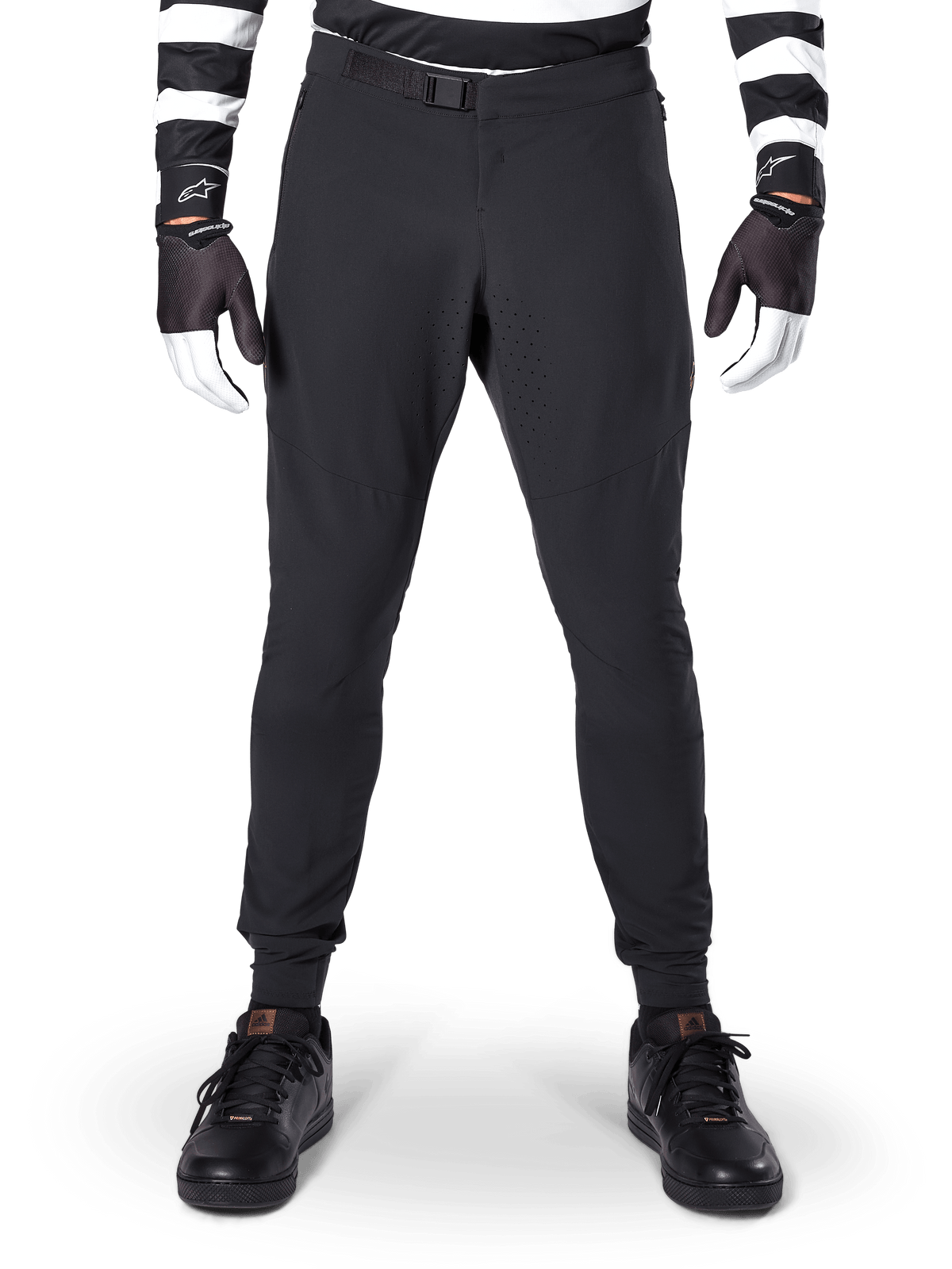 Alpinestars A-Aria Elite bukser, mountainbike-bukser, sort, set forfra med laserperforeringer og magnetisk spændelukning, bæres med en sort- og hvidstribet trøje og sorte handsker, performance-cykeludstyr til trailkørsel