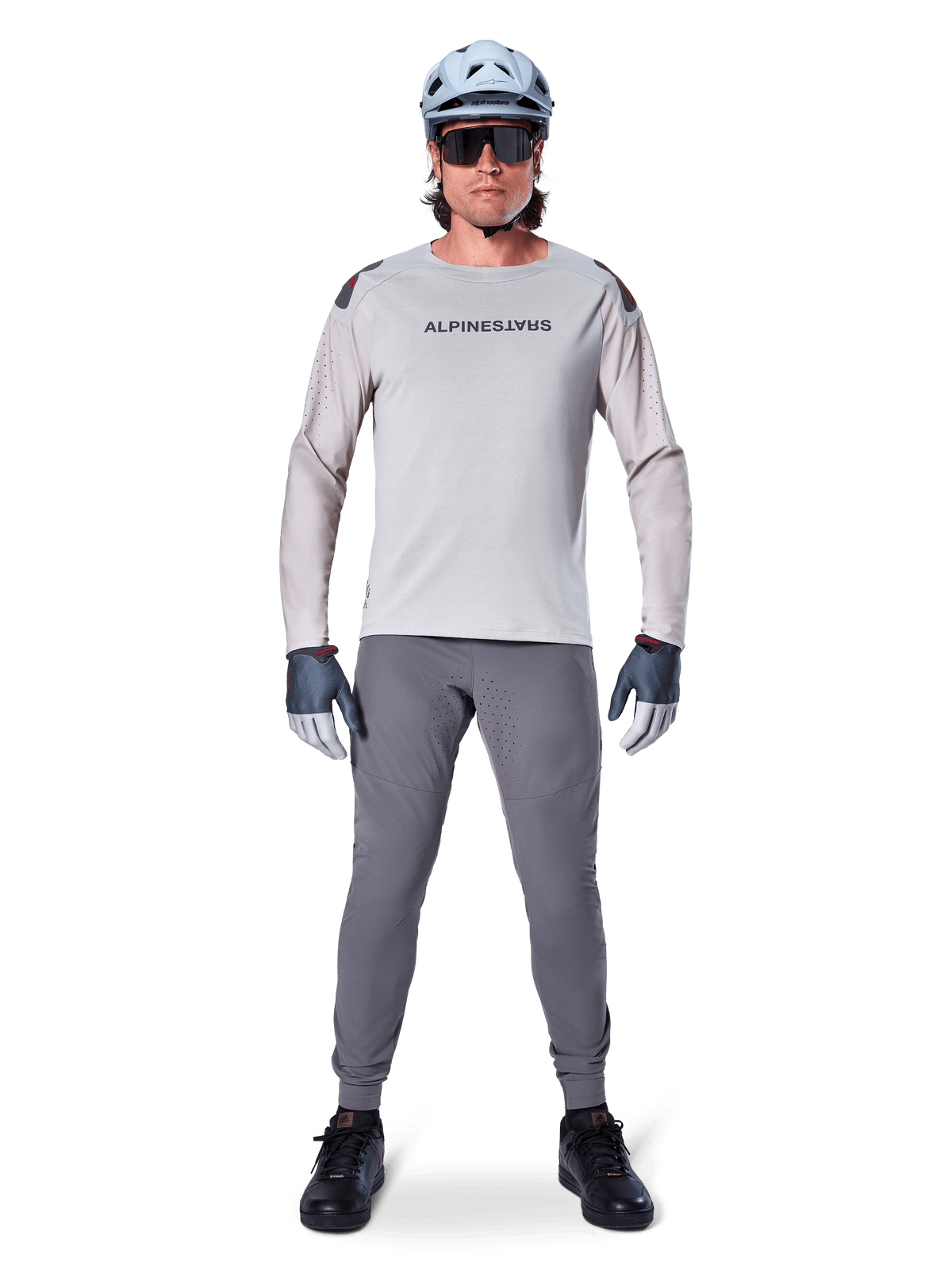 Alpinestars A-Aria Elite bukser, mørkegrå mountainbike-bukser, båret af en rytter i en lysegrå langærmet trøje, lyseblå hjelm og sorte sko, med synlige laserperforeringer på indersiden af benene og en tætsiddende ydelsespasform.