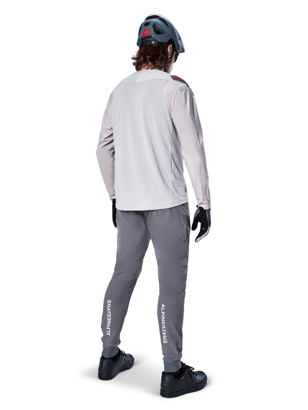 Alpinestars A-Aria Elite bukser, MTB cykelbukser, mørkegrå, set bagfra af en rytter iført et komplet outfit, med hvid Alpinestars-branding på underbenene, performance-pasform med laserperforeringer, kombineret med en lysegrå langærmet trøje og grå MTB-hjelm