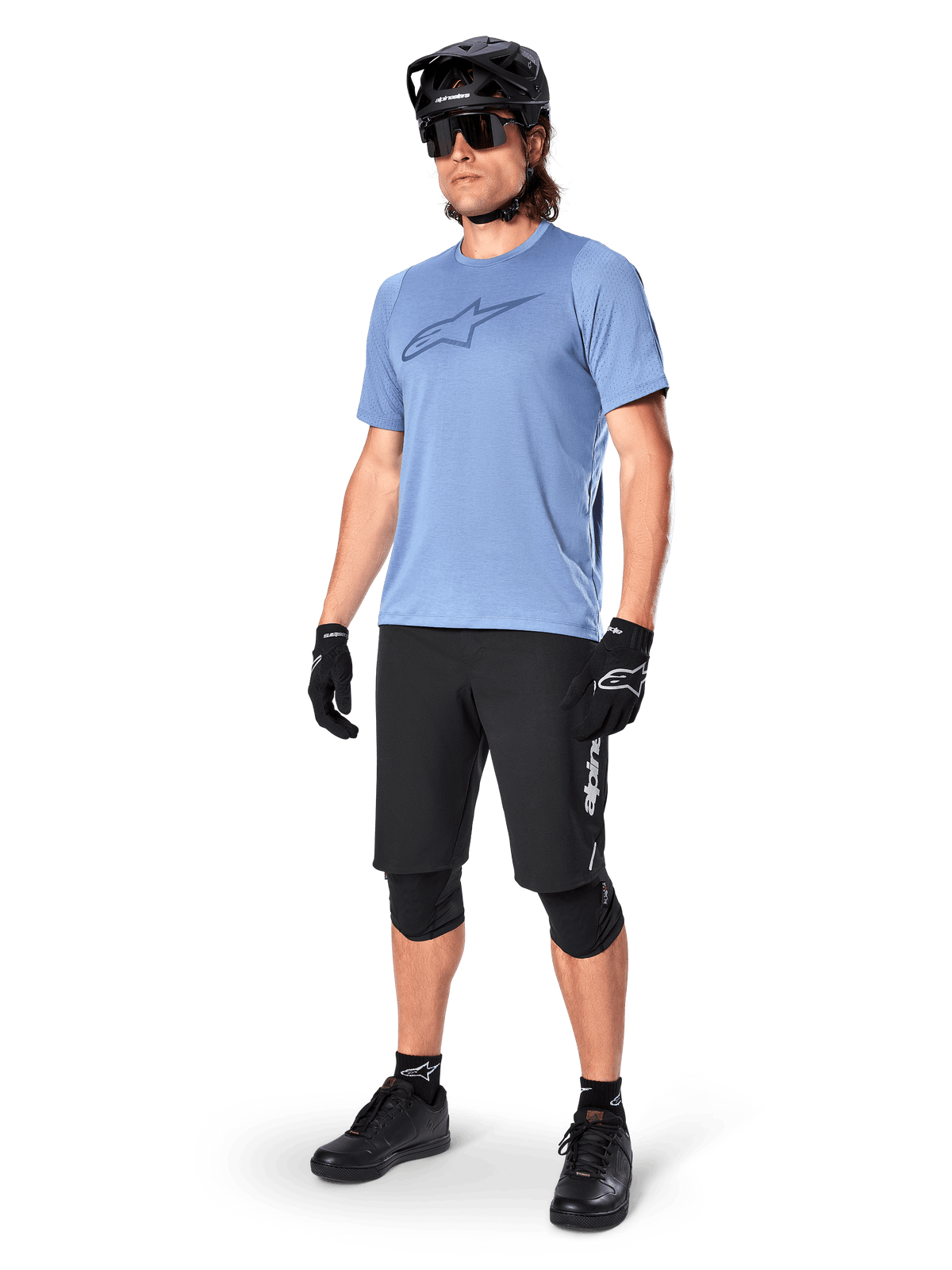 Mandlig rytter iført Alpinestars A-Dura Elite Shorts i sort, lyseblå kortærmet jersey med brystlogo, sort hjelm, solbriller og beskyttende knæpuder, komplet mountainbike-udstyr til terrænkørsel.