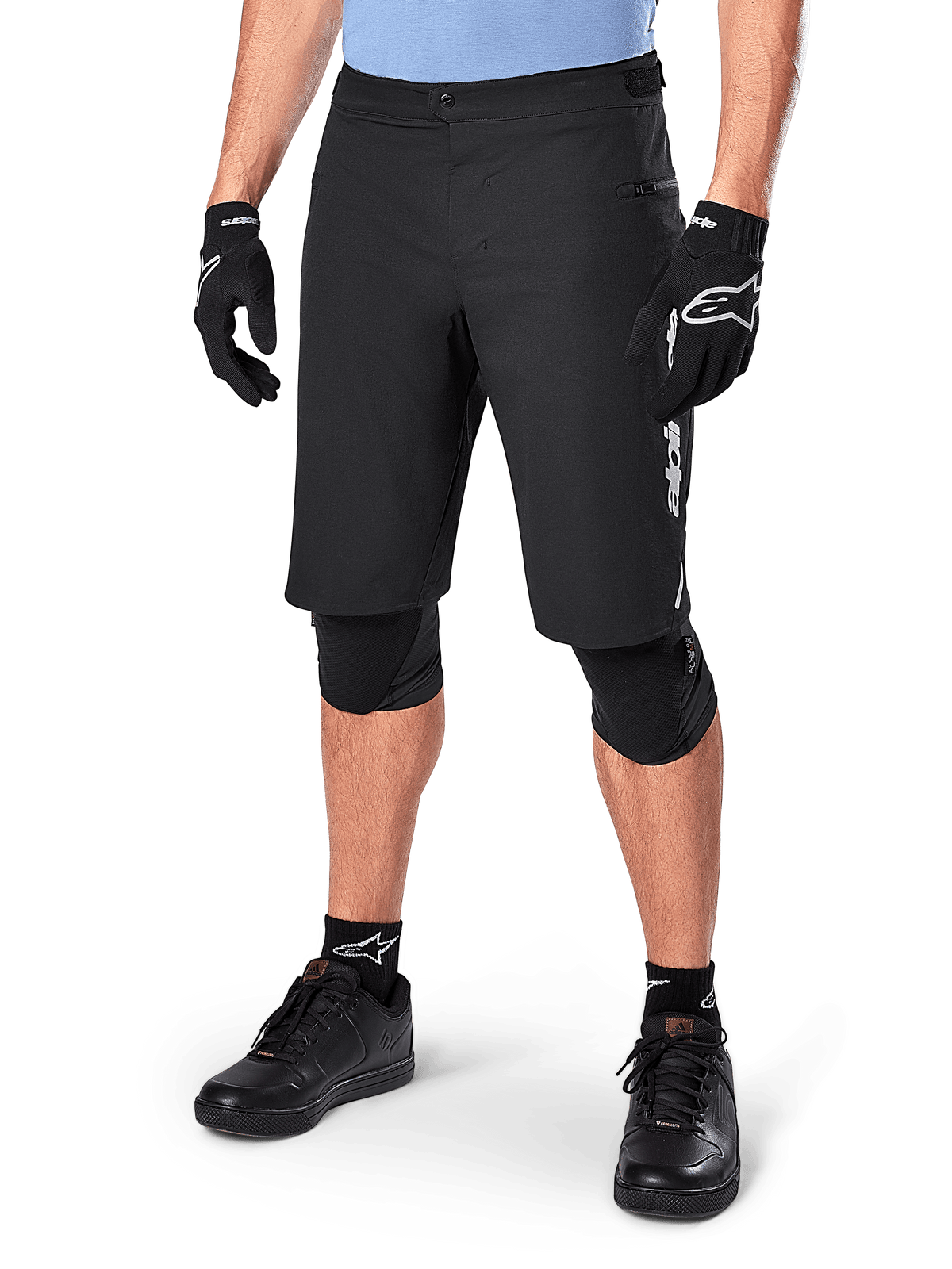 Alpinestars A-Dura Elite Shorts, sorte MTB-shorts til mountainbike, vist med lyseblå trøje og sort knæbeskyttelse, har sikker trykknaplukning og lynlåslomme, parret med sorte cykelsko og handsker for et komplet off-road outfit.