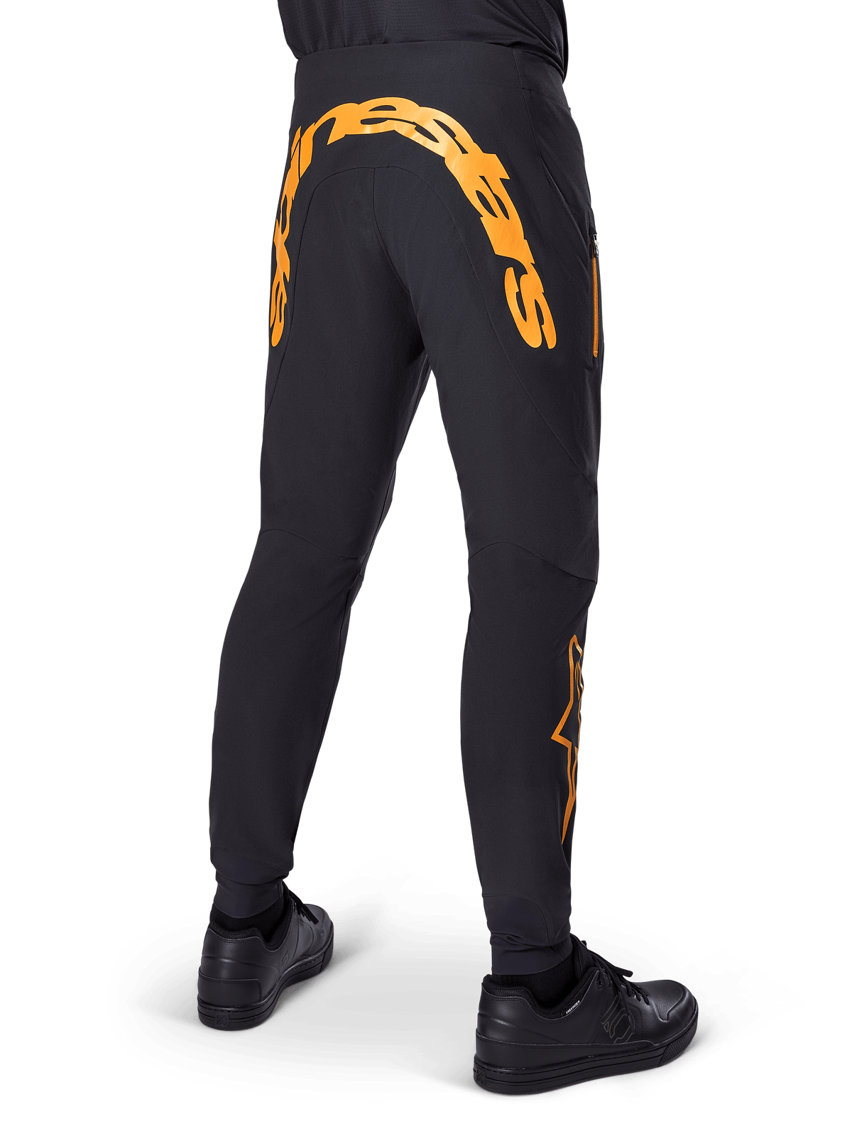 Alpinestars A-Supra Race Pants, Black MTB Pants, Rear view featuring large orange Alpinestars wordmark across the back yoke, orange logo on the lower leg, performance fit with zippered pocket, worn with black shoes